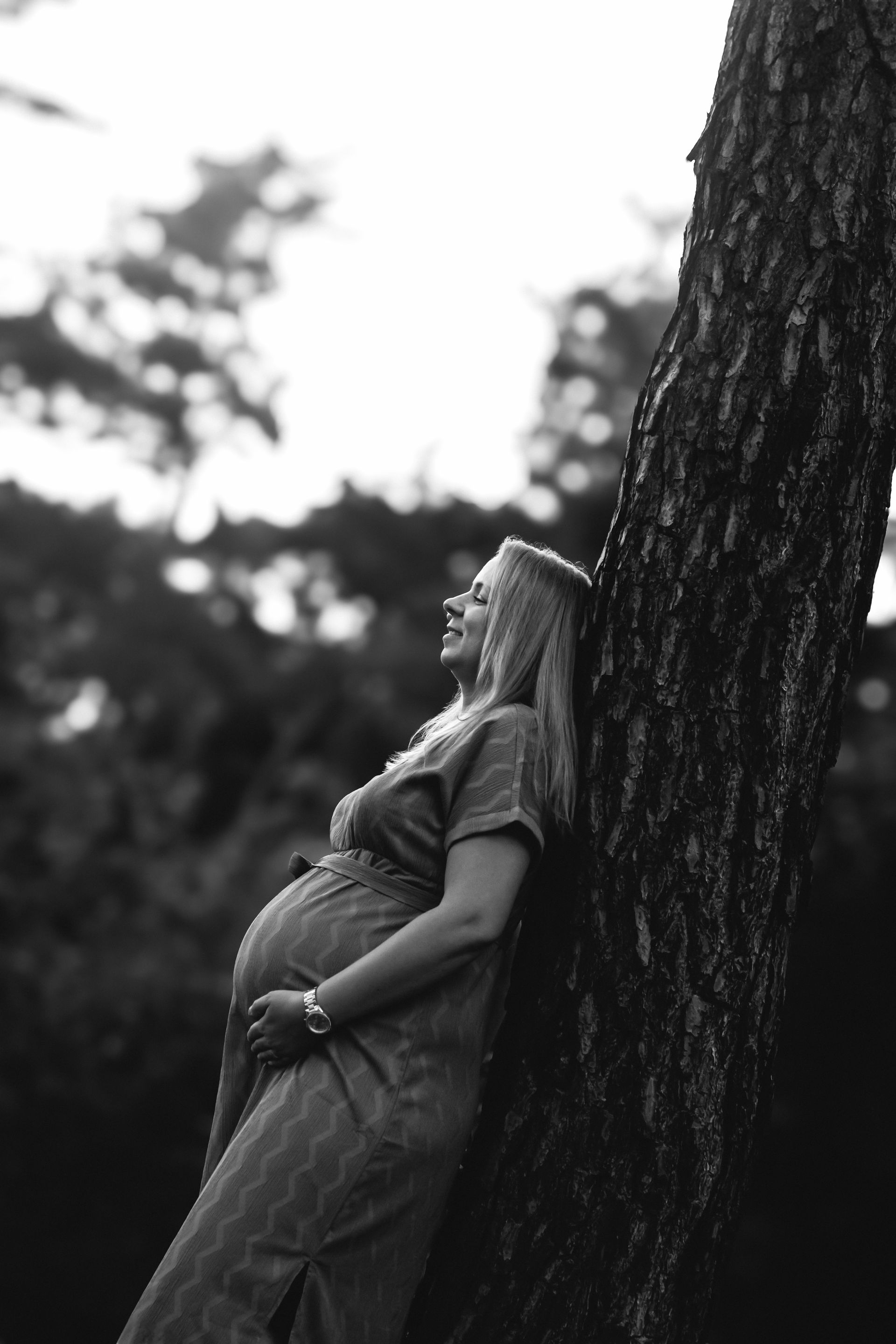 Op een zwart-witfoto leunt een zwangere vrouw tegen een boom.