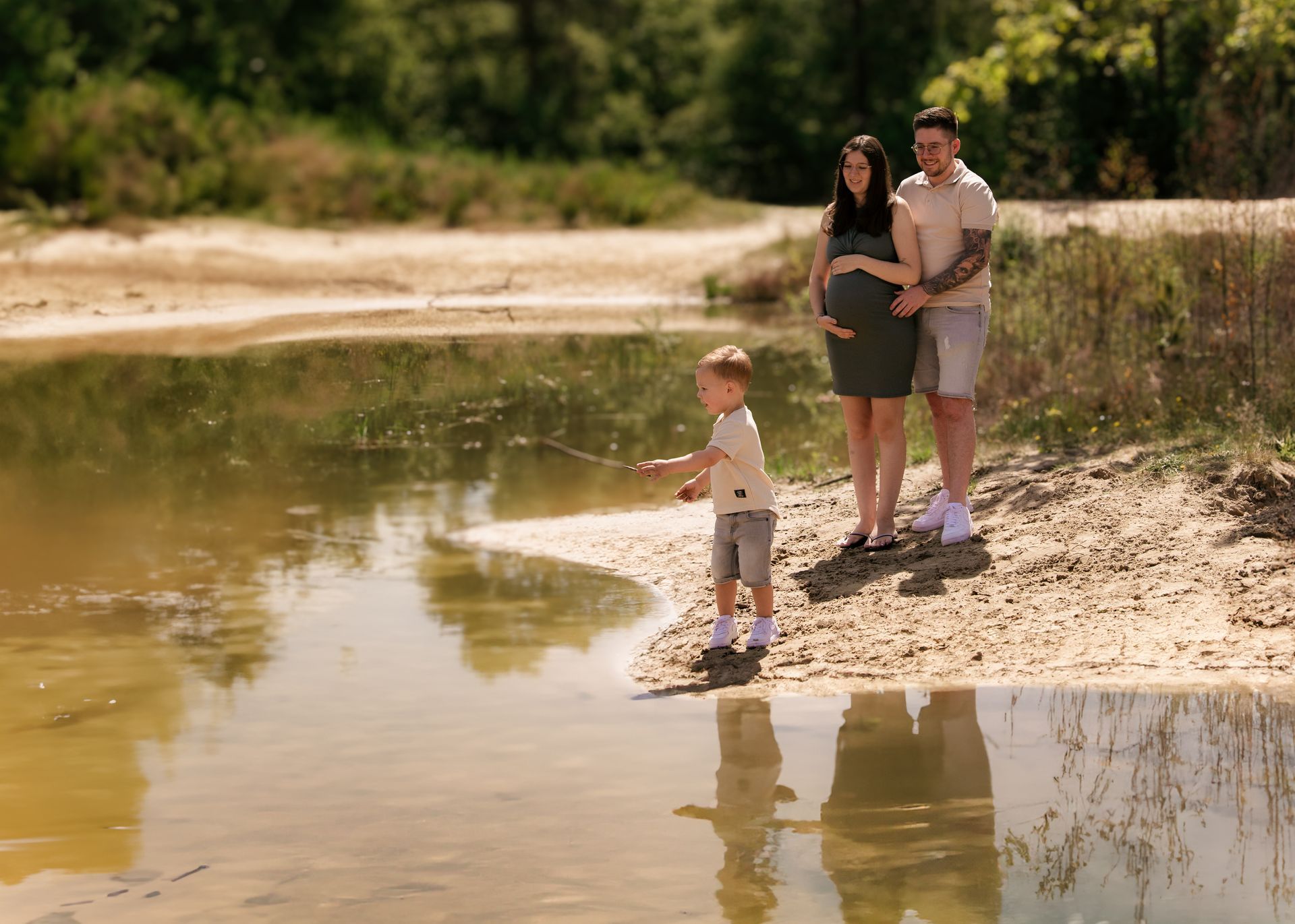 Een zwangere vrouw, een man en een kind vissen in een meer.