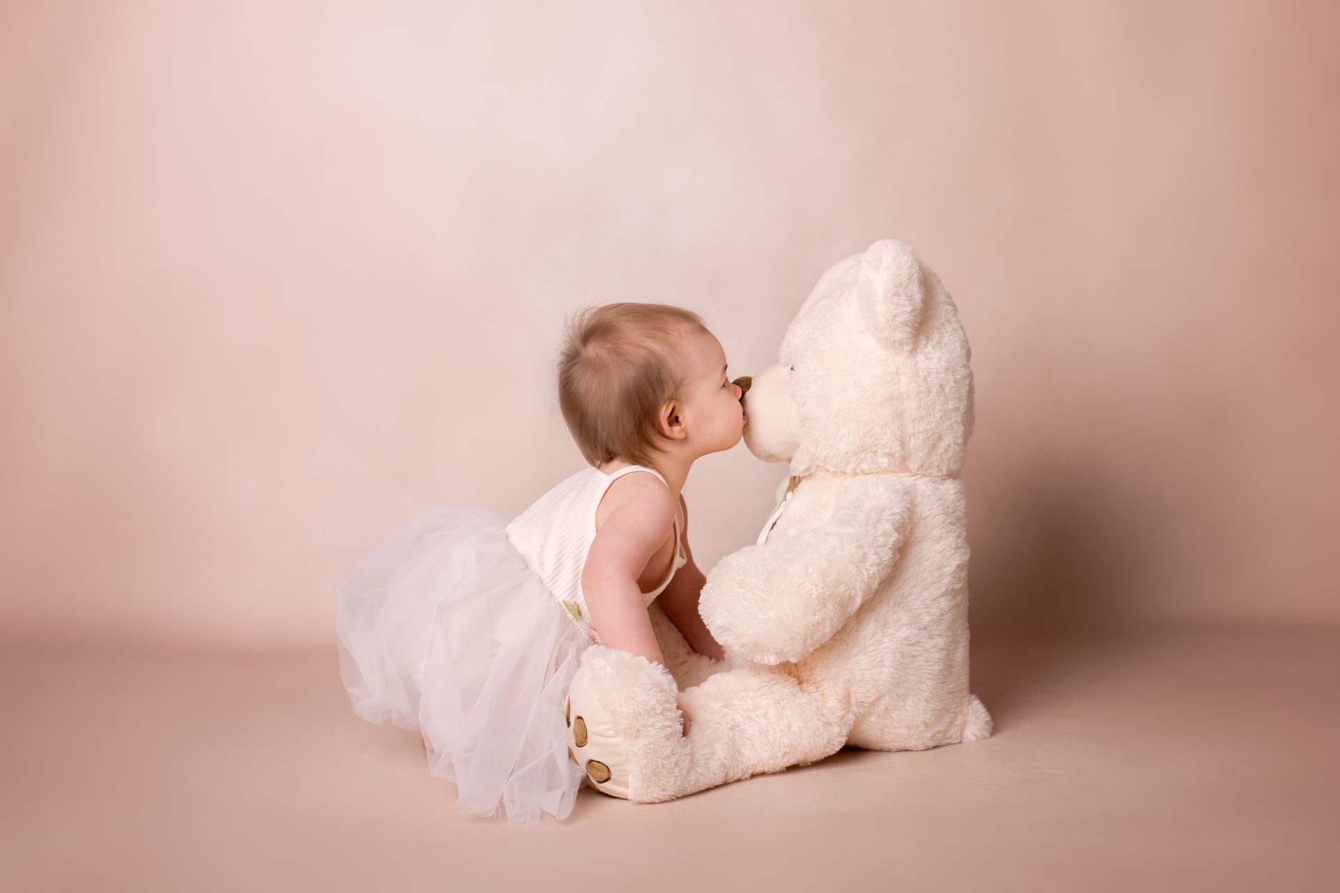 Een baby kust een teddybeer op de neus.