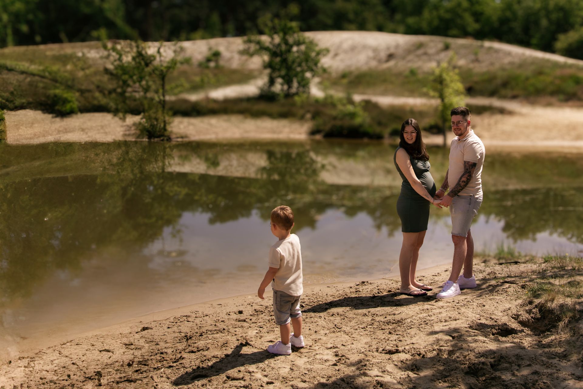 Een zwangere vrouw, een man en een kind staan ​​op het strand bij een meer.