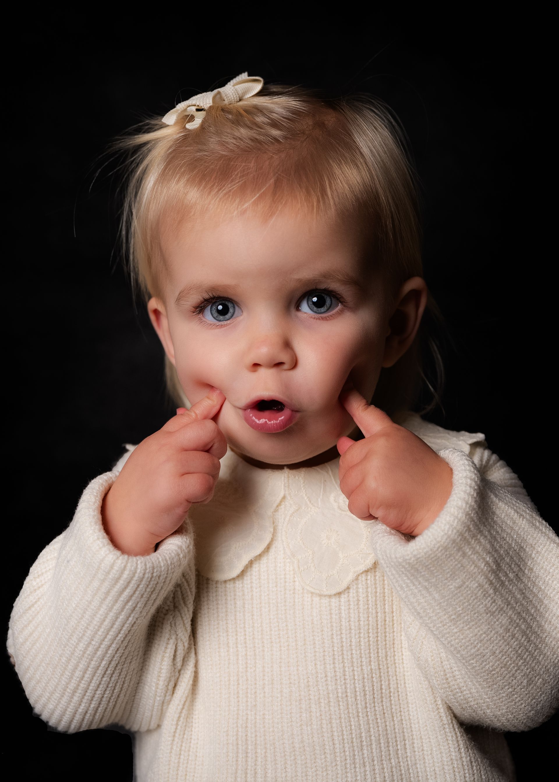 Een klein meisje in een witte trui trekt een grappig gezicht.