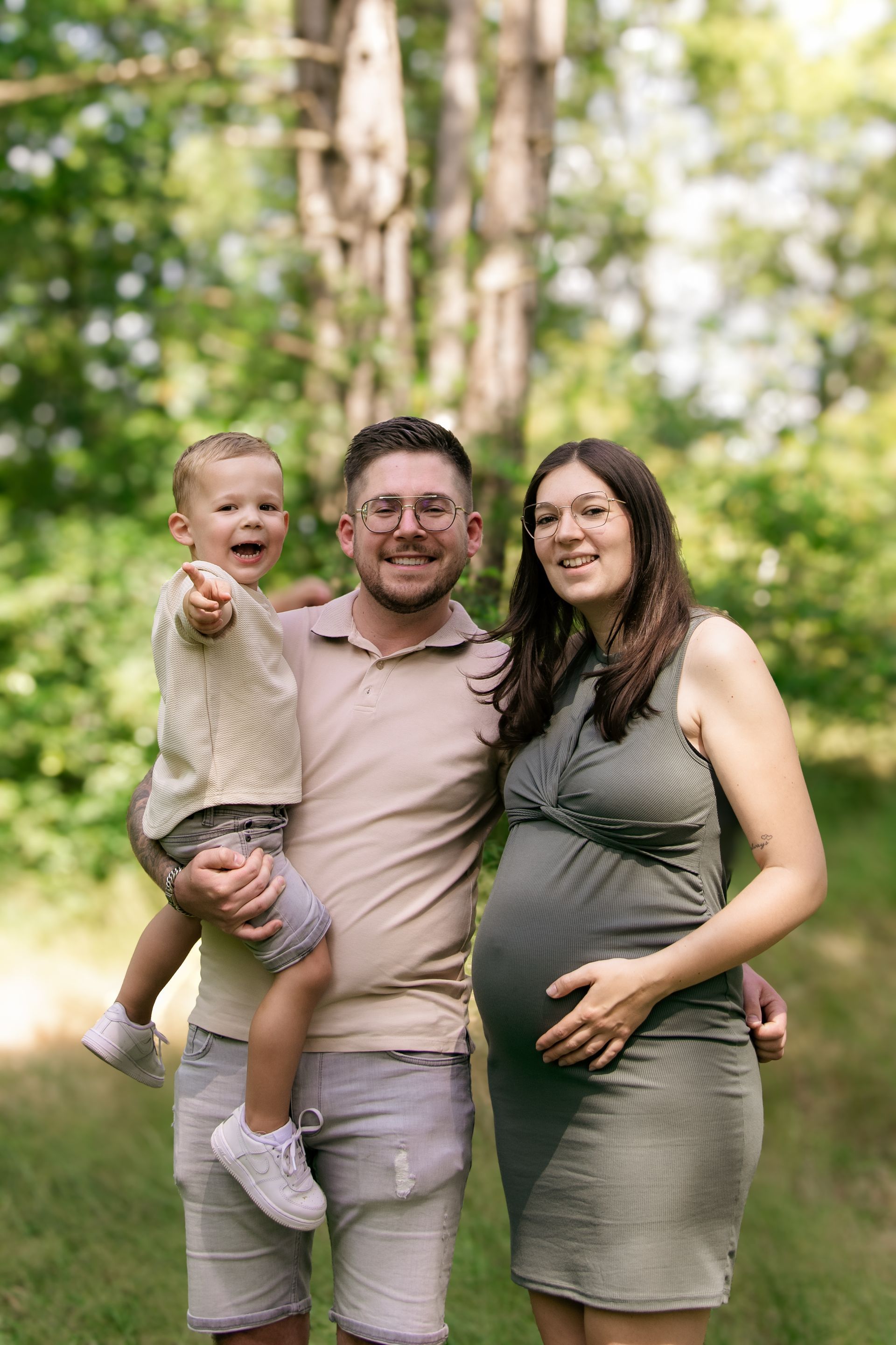 Een zwangere vrouw, een man en een kind poseren voor een foto in een park.
