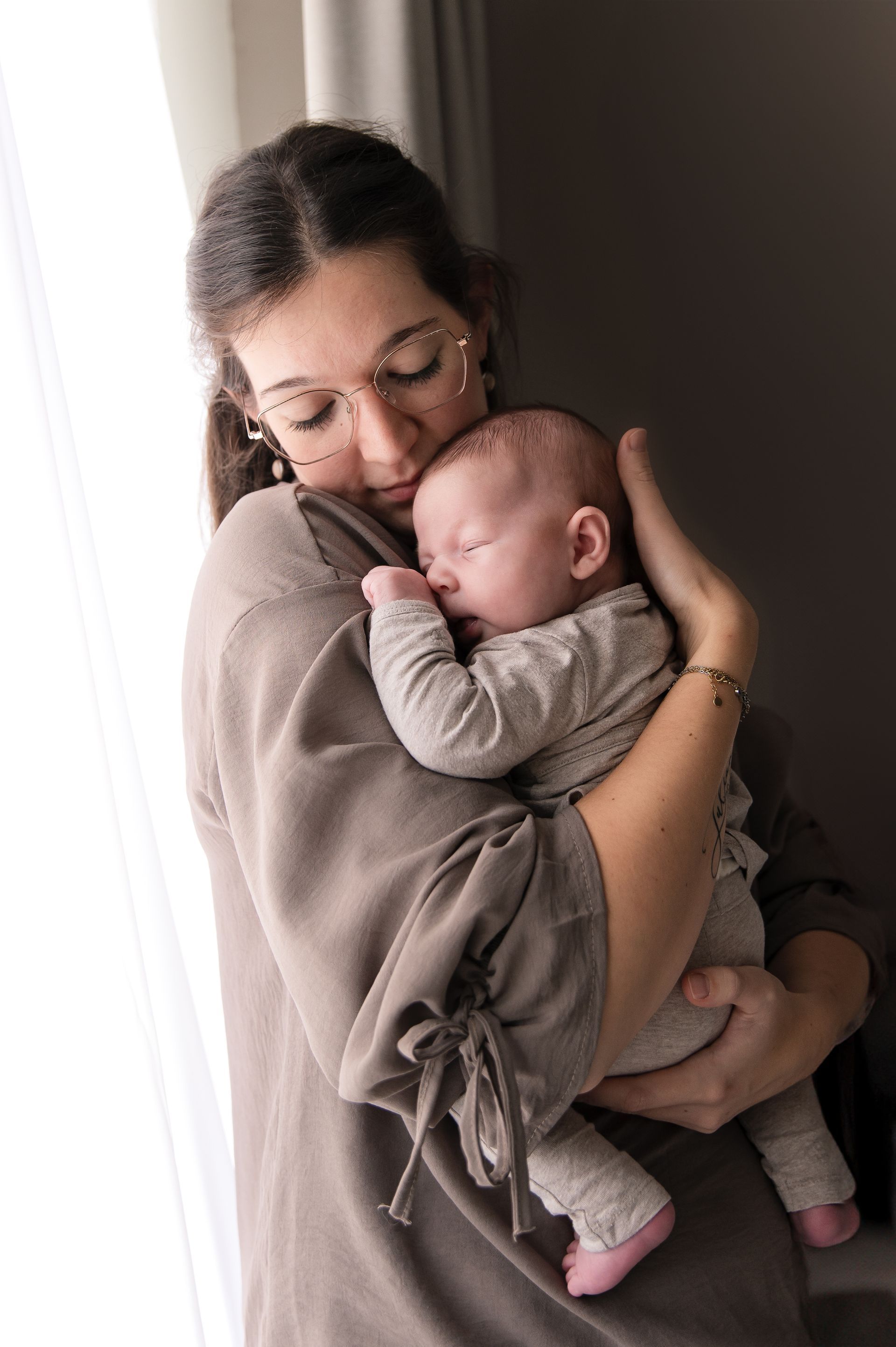 Een vrouw houdt een baby in haar armen voor een raam.