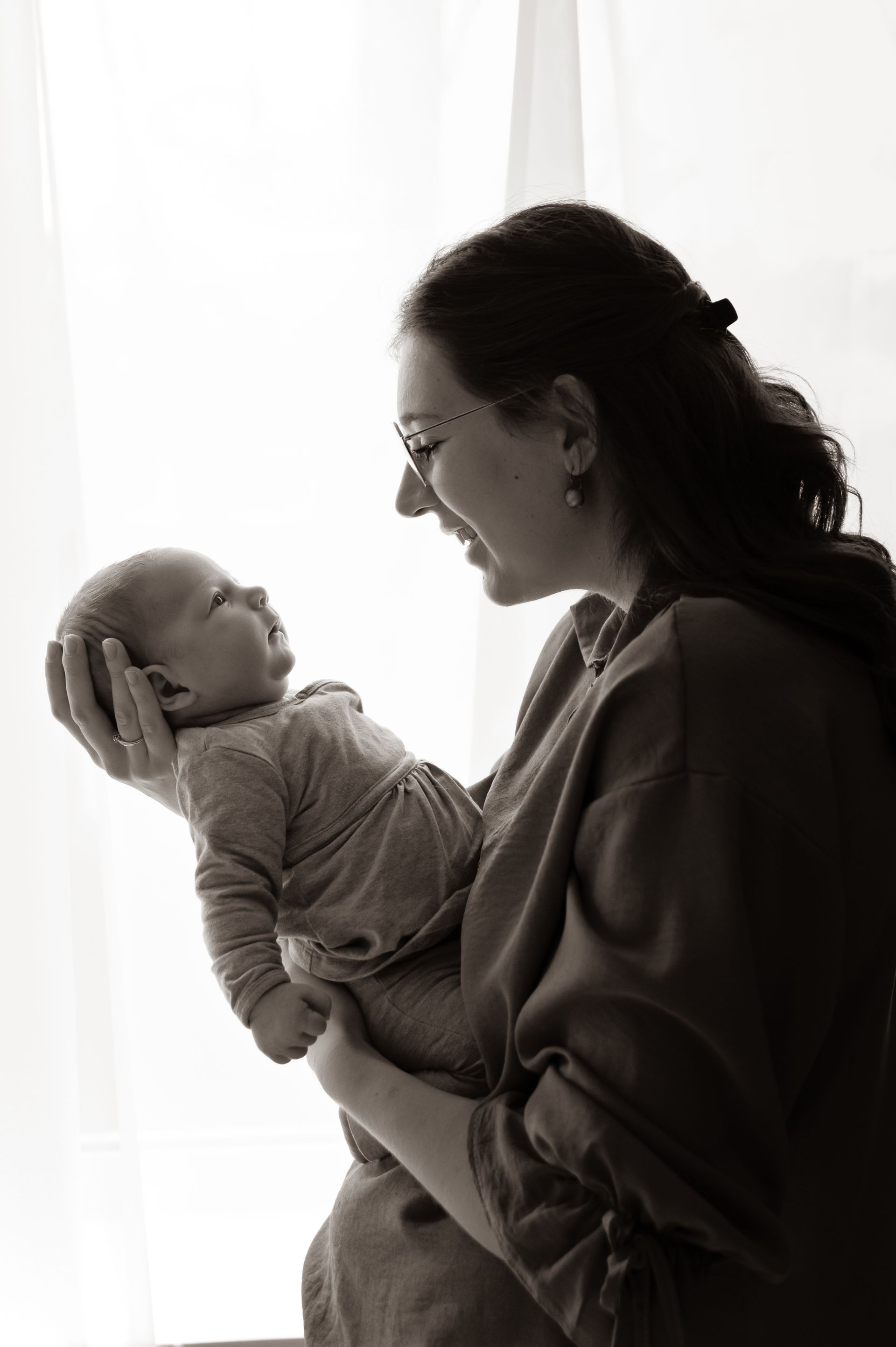 Een vrouw houdt een baby in haar armen voor een raam.