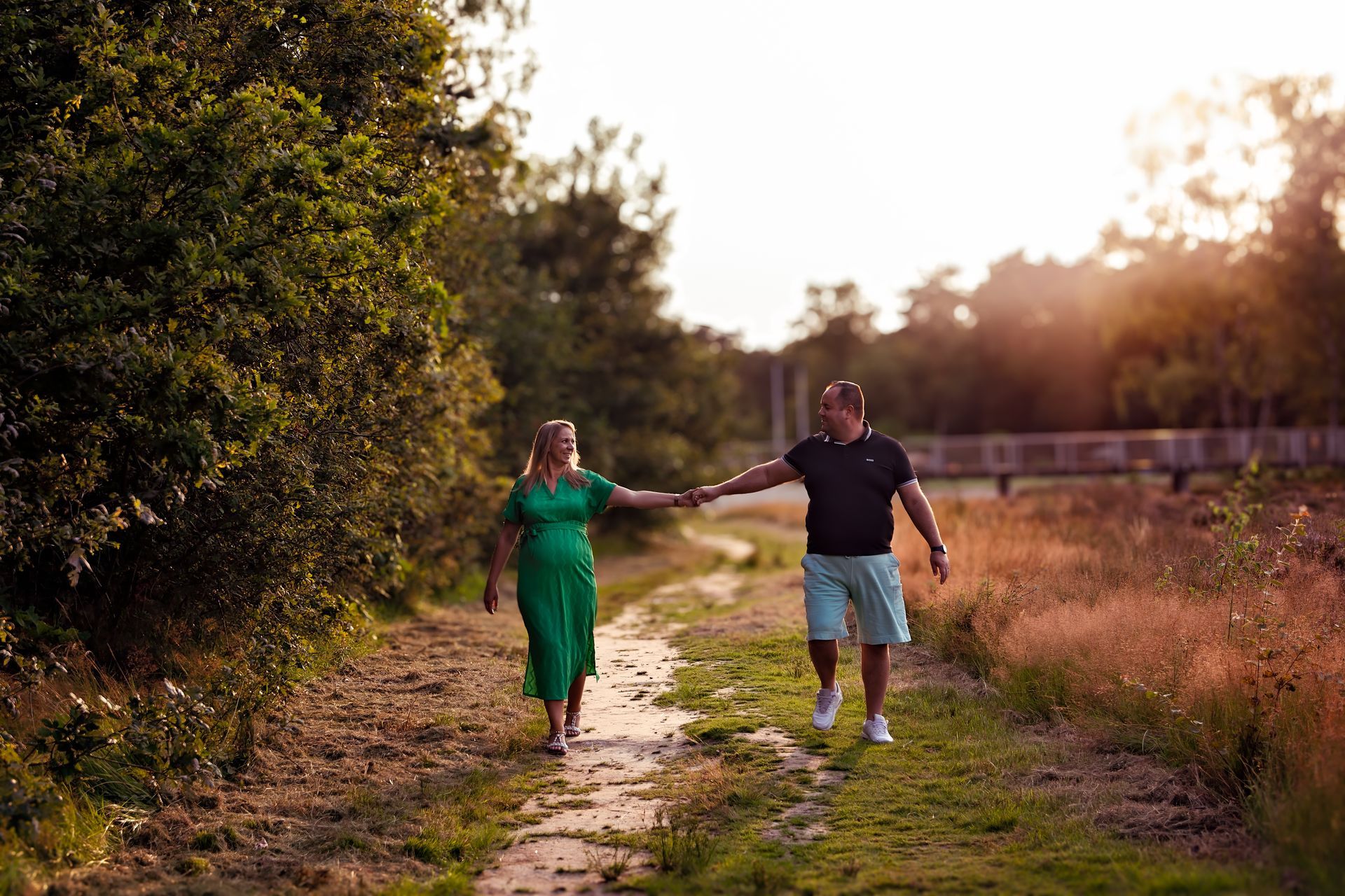 Een man en een zwangere vrouw lopen hand in hand over een pad.