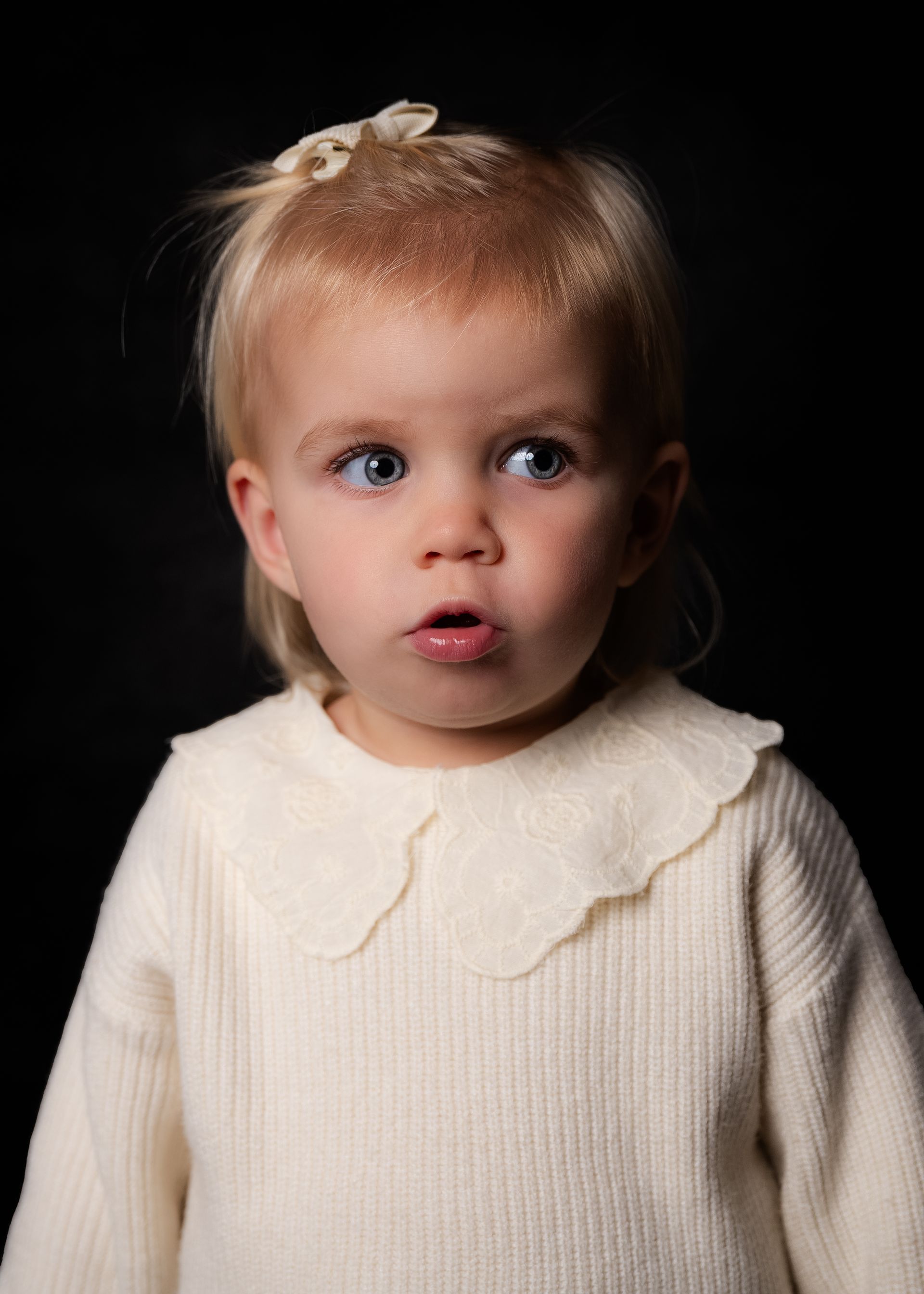 Een klein meisje draagt ​​een witte trui en een strik in haar haar.