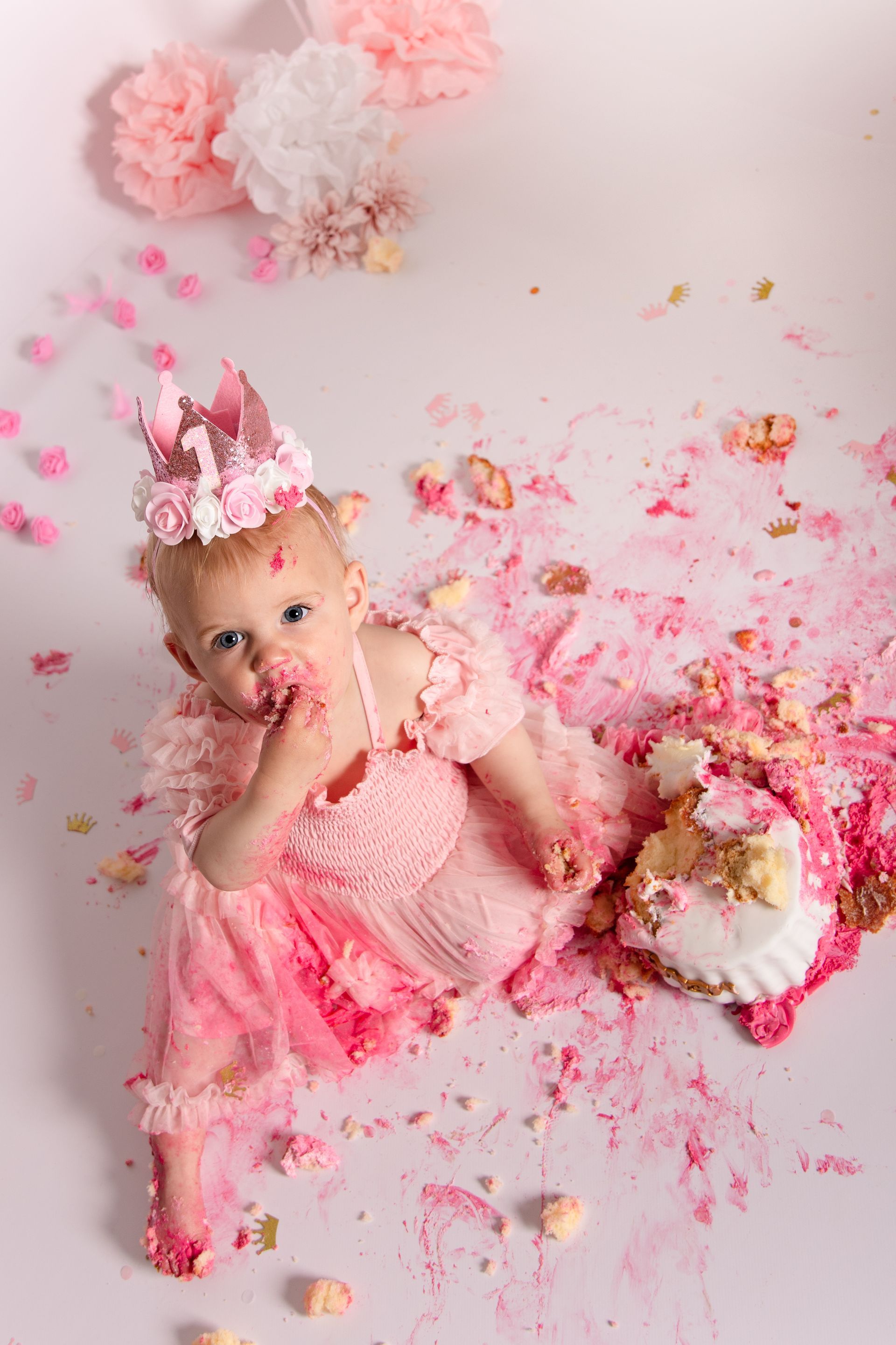 Een babymeisje in een roze jurk eet een roze taart.