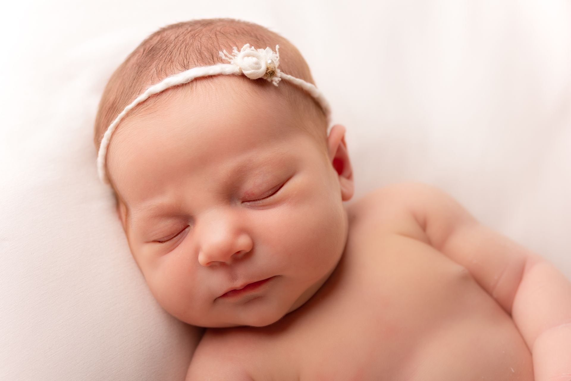 Een pasgeboren babymeisje met een witte haarband slaapt op een witte deken.