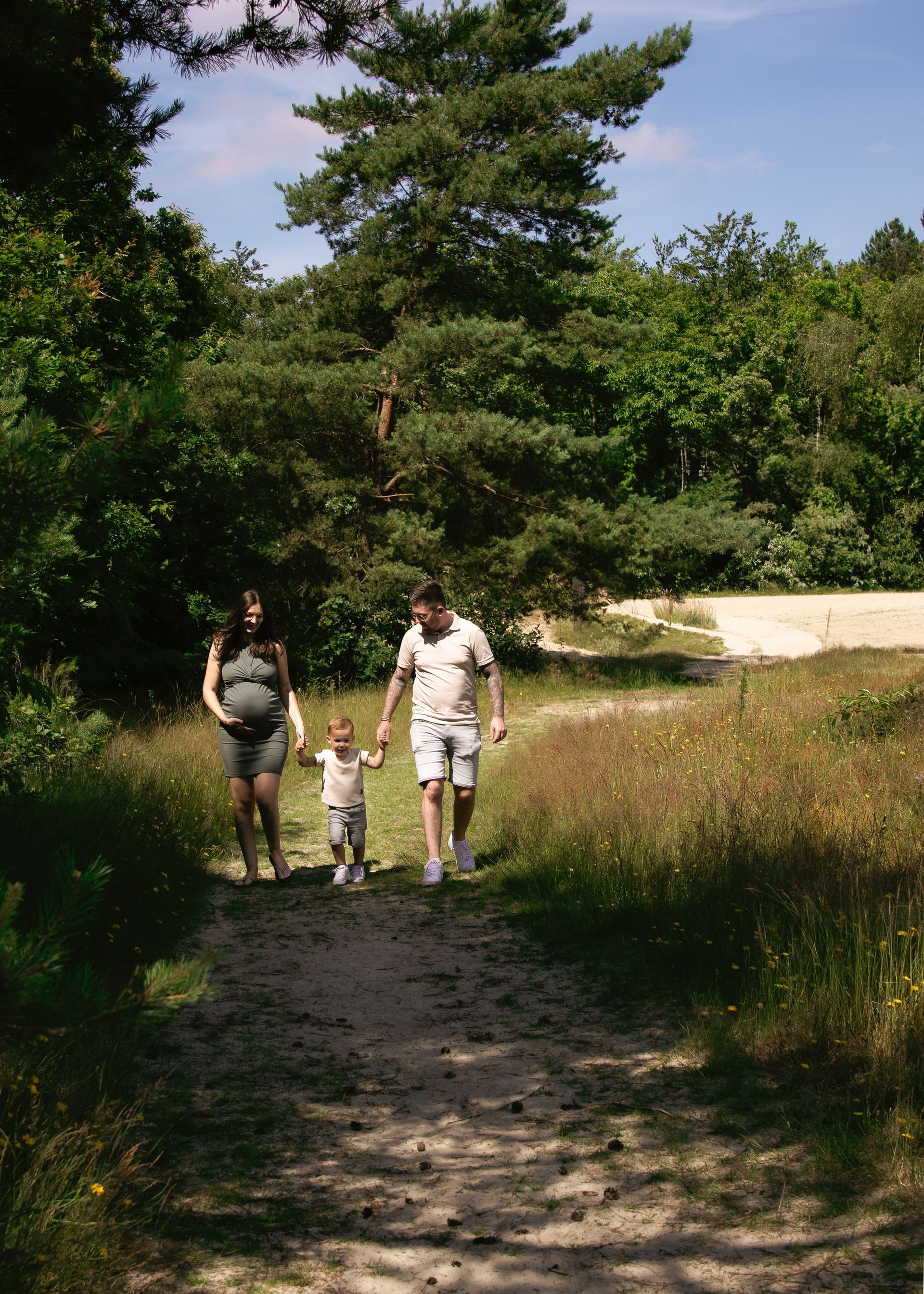 Een zwangere vrouw, een man en een kind lopen over een zandpad.