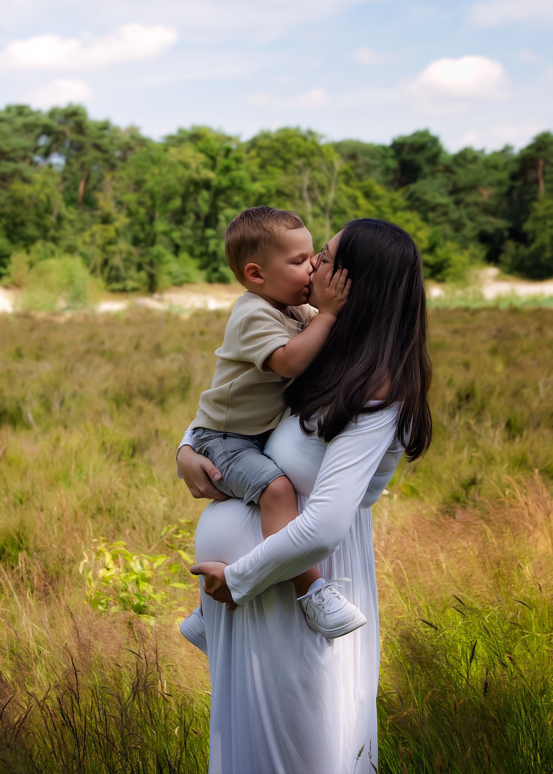 Een zwangere vrouw kust haar zoon op de wang in een veld.