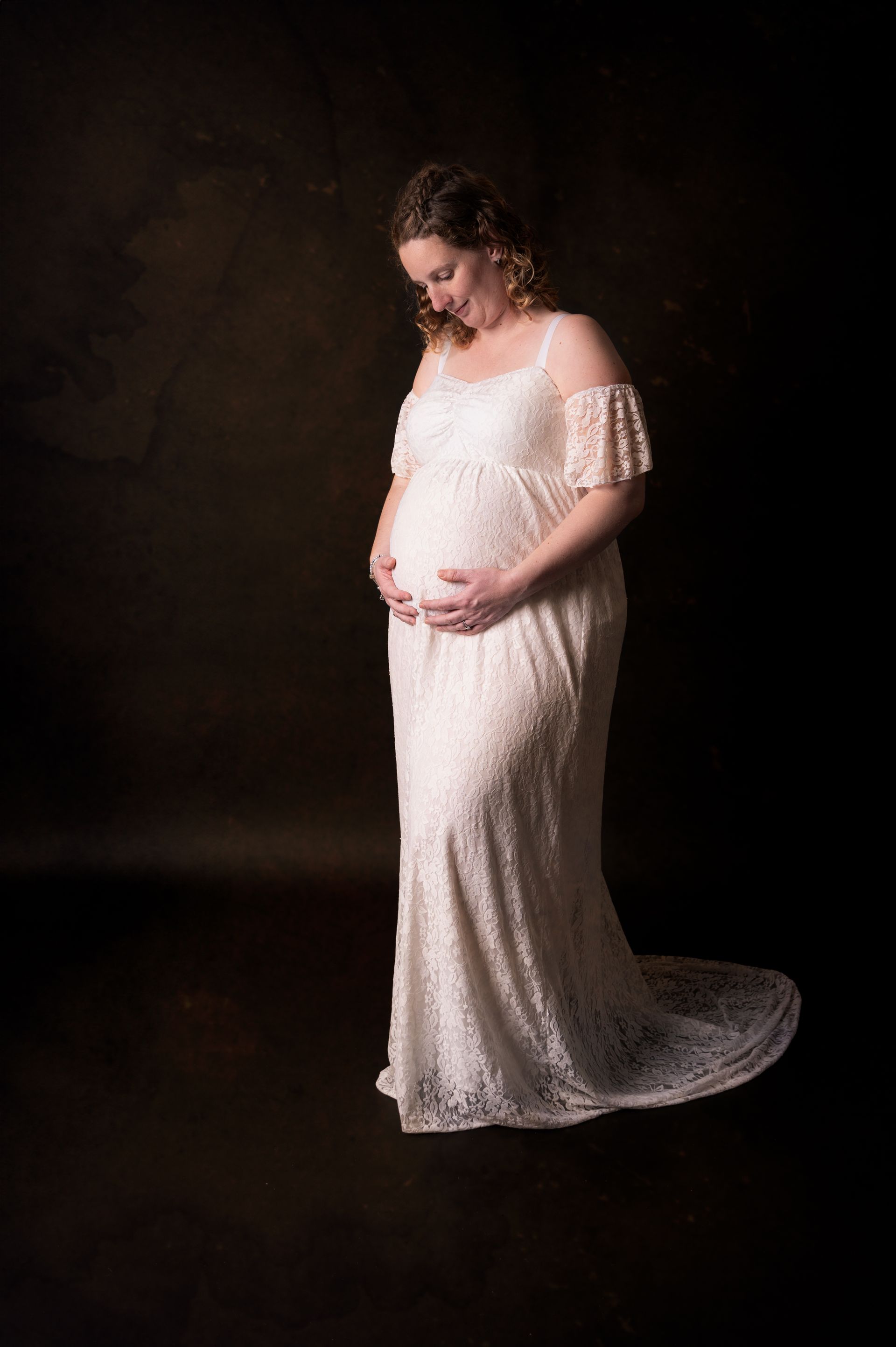 Een zwangere vrouw in een witte kanten jurk houdt haar buik vast.