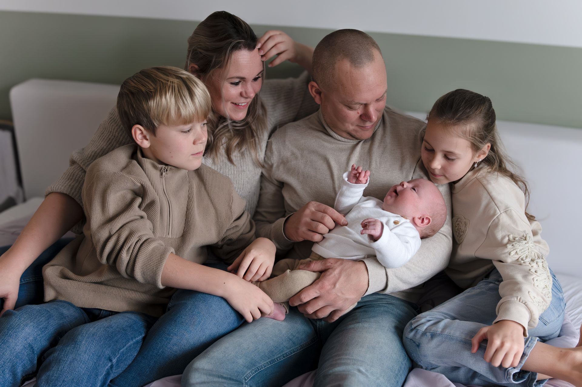 Een gezin zit op een bed met een pasgeboren baby.