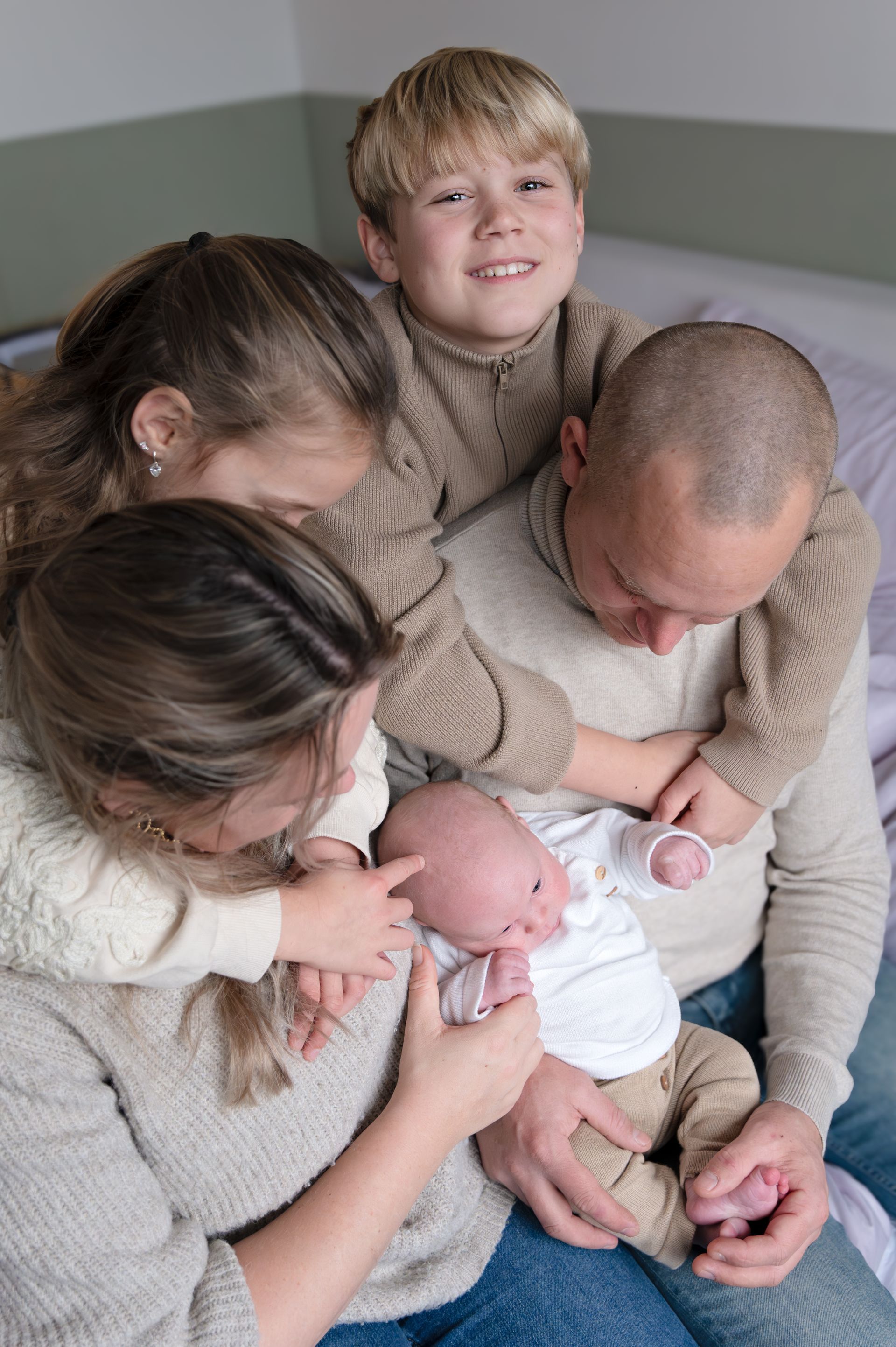 Een gezin zit op een bed met een pasgeboren baby.