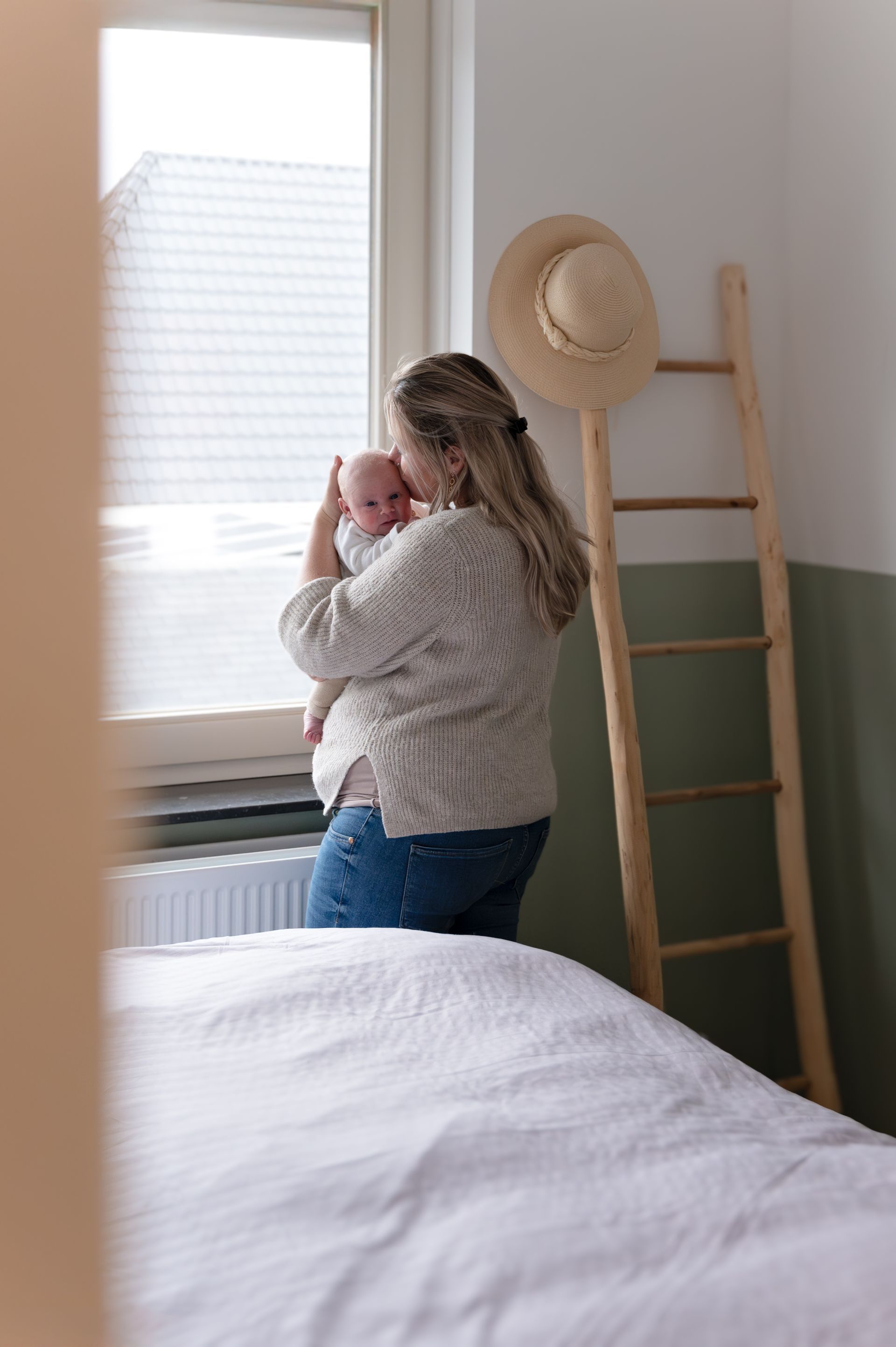 Een vrouw houdt een baby in haar armen en kijkt uit het raam.