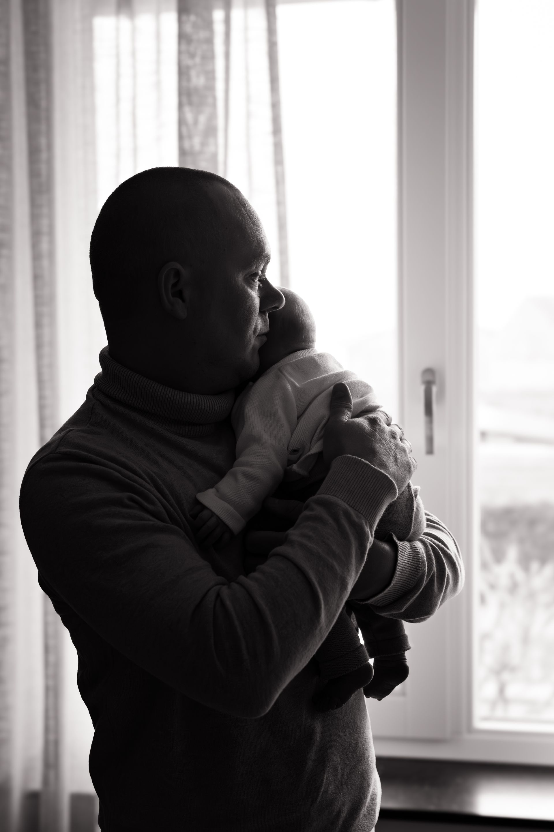 Een man houdt een baby in zijn armen voor een raam.