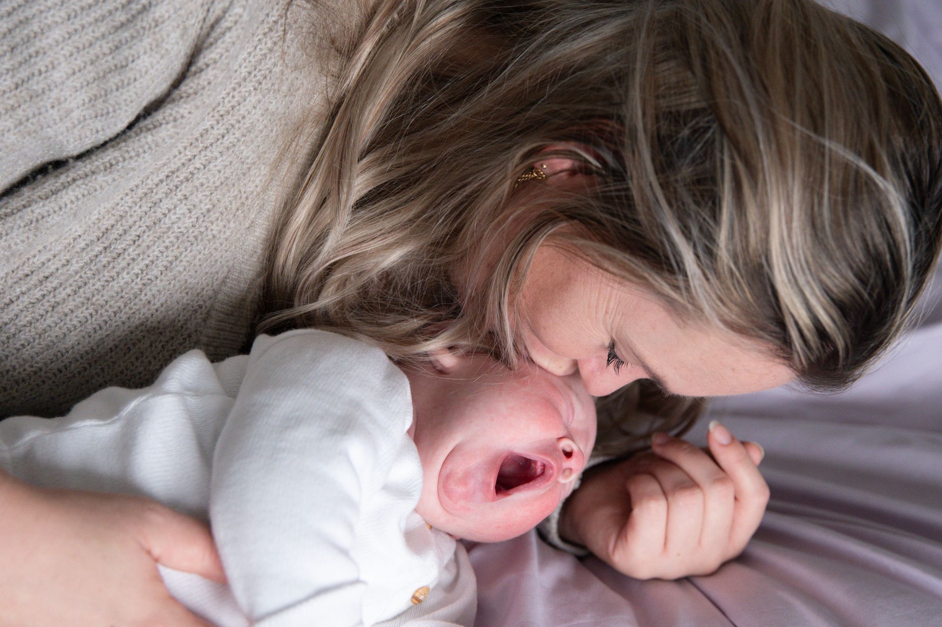 Een vrouw ligt op een bed met een huilende baby in haar armen.