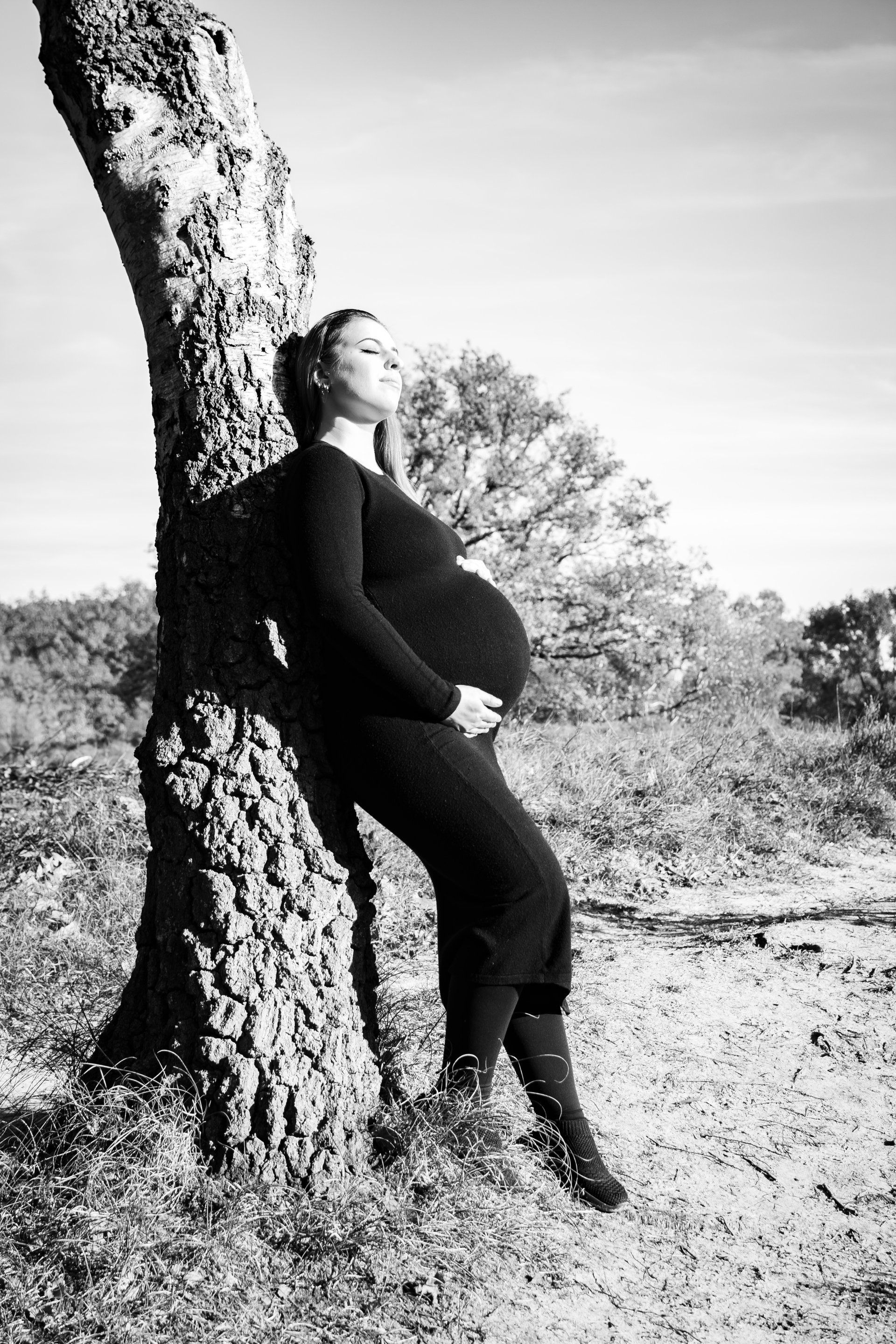 Op een zwart-witfoto leunt een zwangere vrouw tegen een boom.