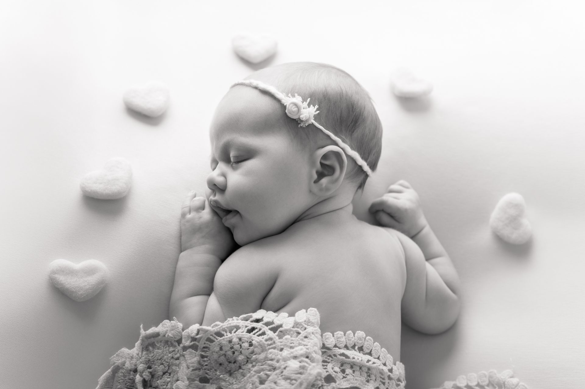 Zwart-witfoto van een slapende pasgeborene met een bloemenhoofdband, omringd door hartvormige versieringen.