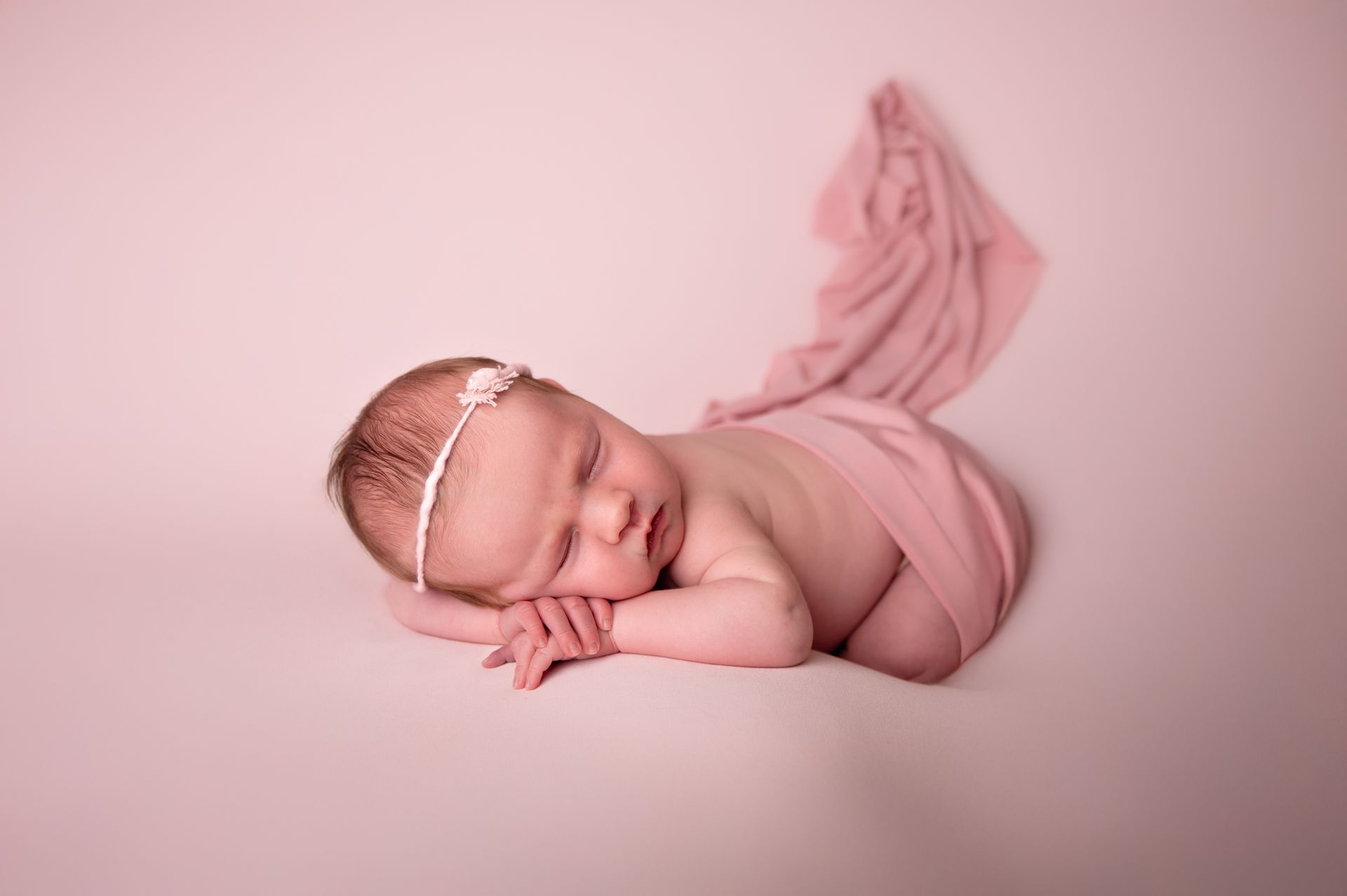 Een pasgeboren baby, gewikkeld in een roze deken, slaapt op een roze achtergrond.