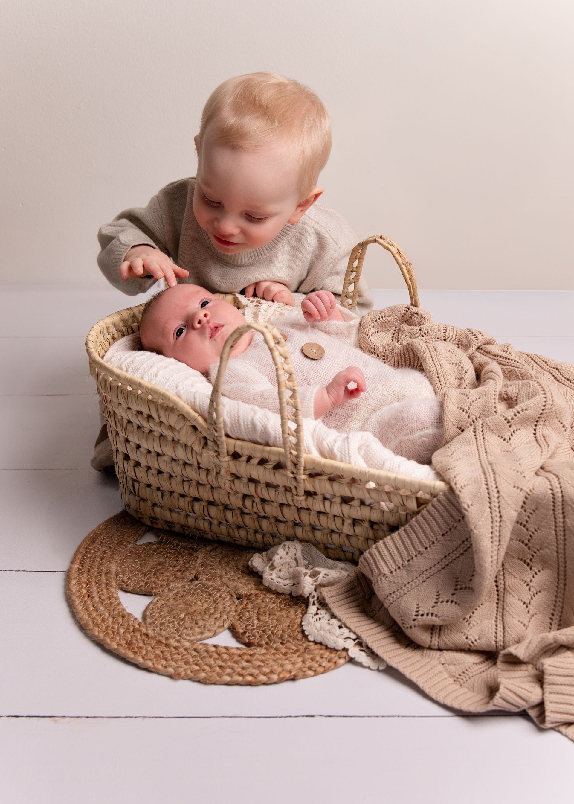 Een jongetje staat naast een baby in een mandje.