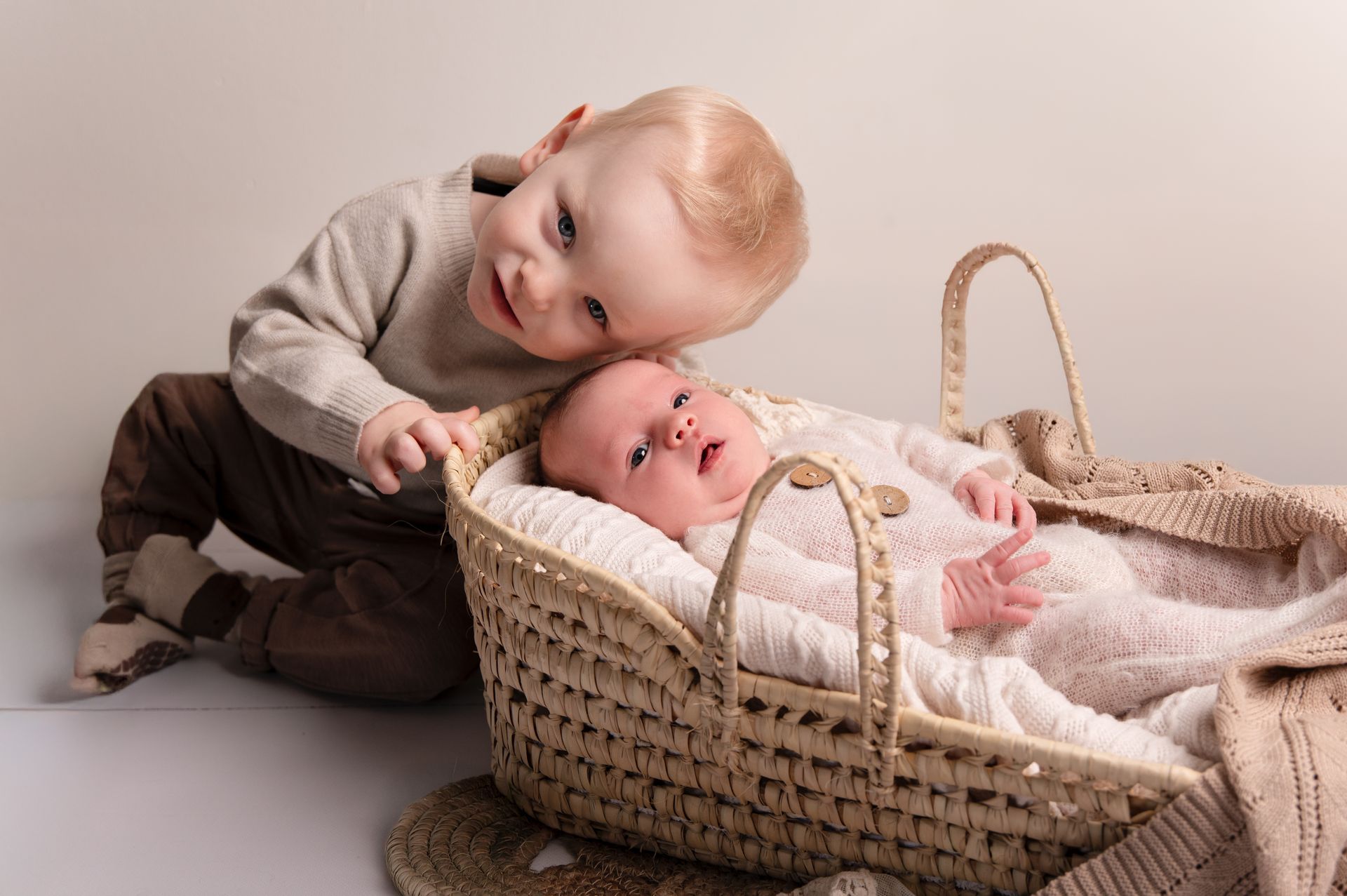 Een jongetje zit naast een baby in een mandje.