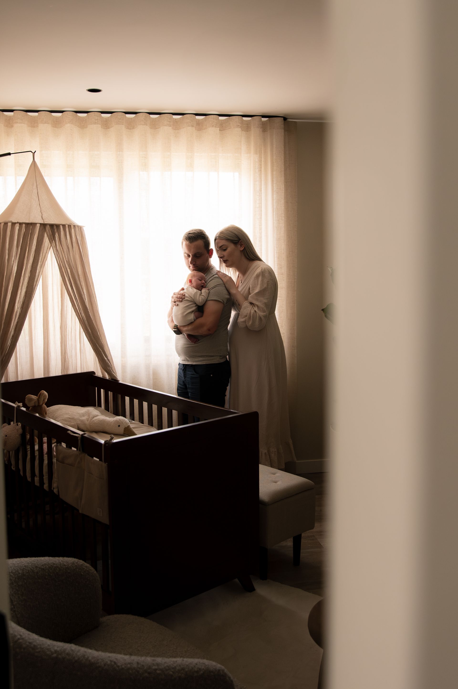 Een stel kijkt naar hun pasgeboren baby in een kinderkamer. De vader houdt de baby vast terwijl de moeder toekijkt, bij de wieg.