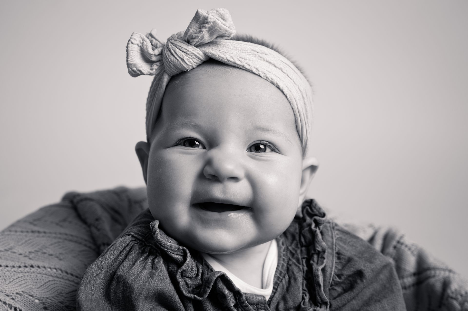Een zwart-witfoto van een baby met een hoofdband om en lachend.