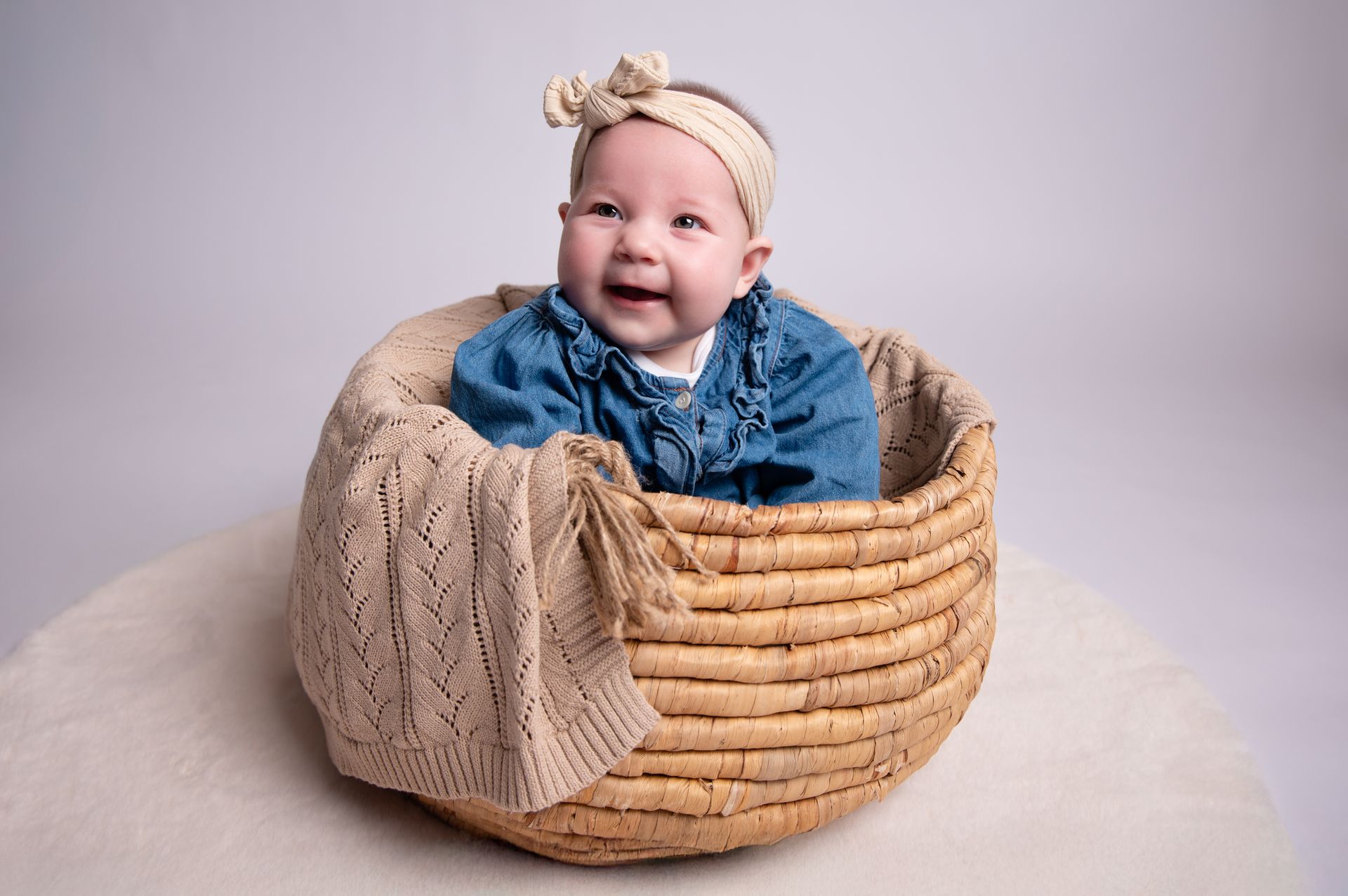 Een baby zit in een rieten mand op een tafel.