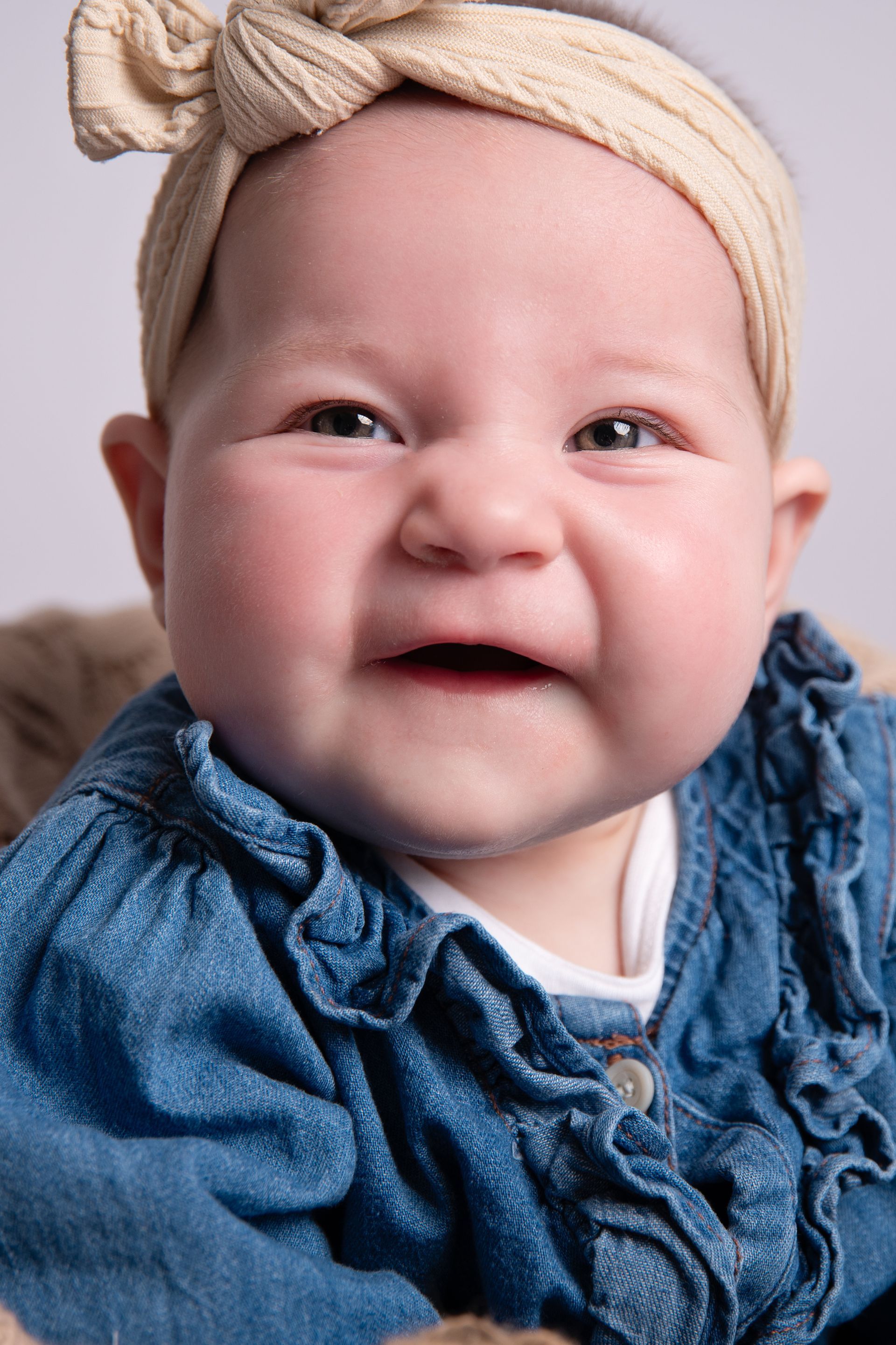 Een baby met een hoofdband en een spijkerjurkje lacht.