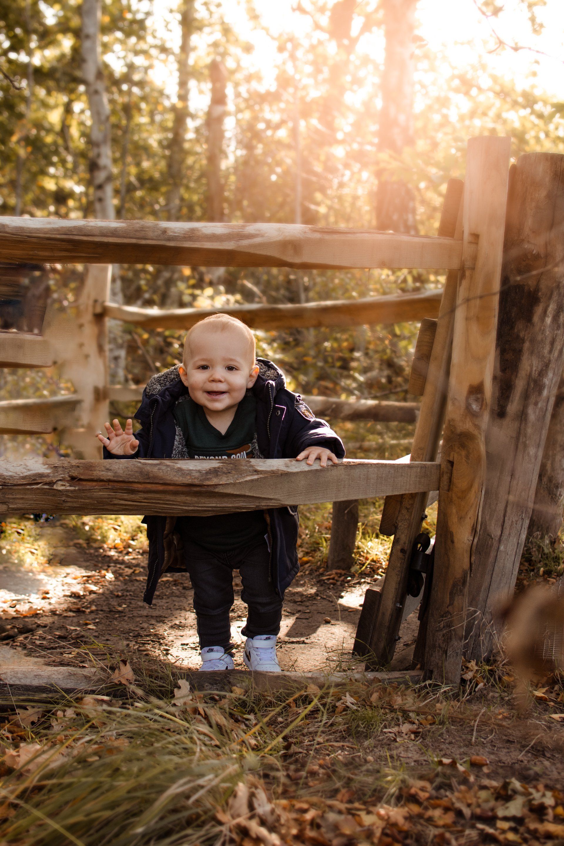 Een baby staat achter een houten hek in het bos.