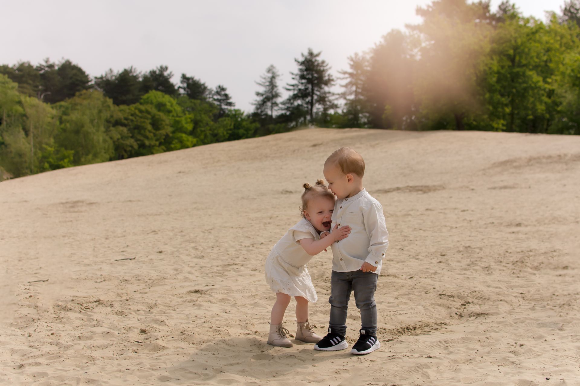 Een jongen en een meisje staan ​​naast elkaar in het zand.