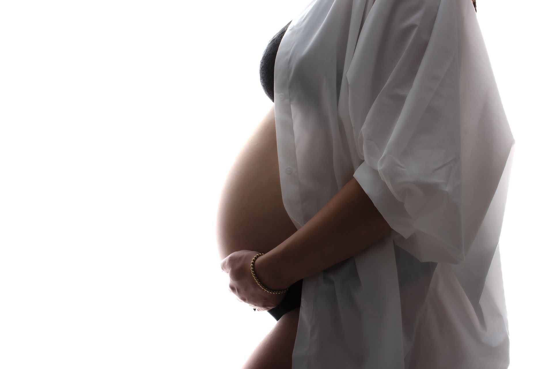 Een zwangere vrouw in een wit gewaad houdt haar buik vast.