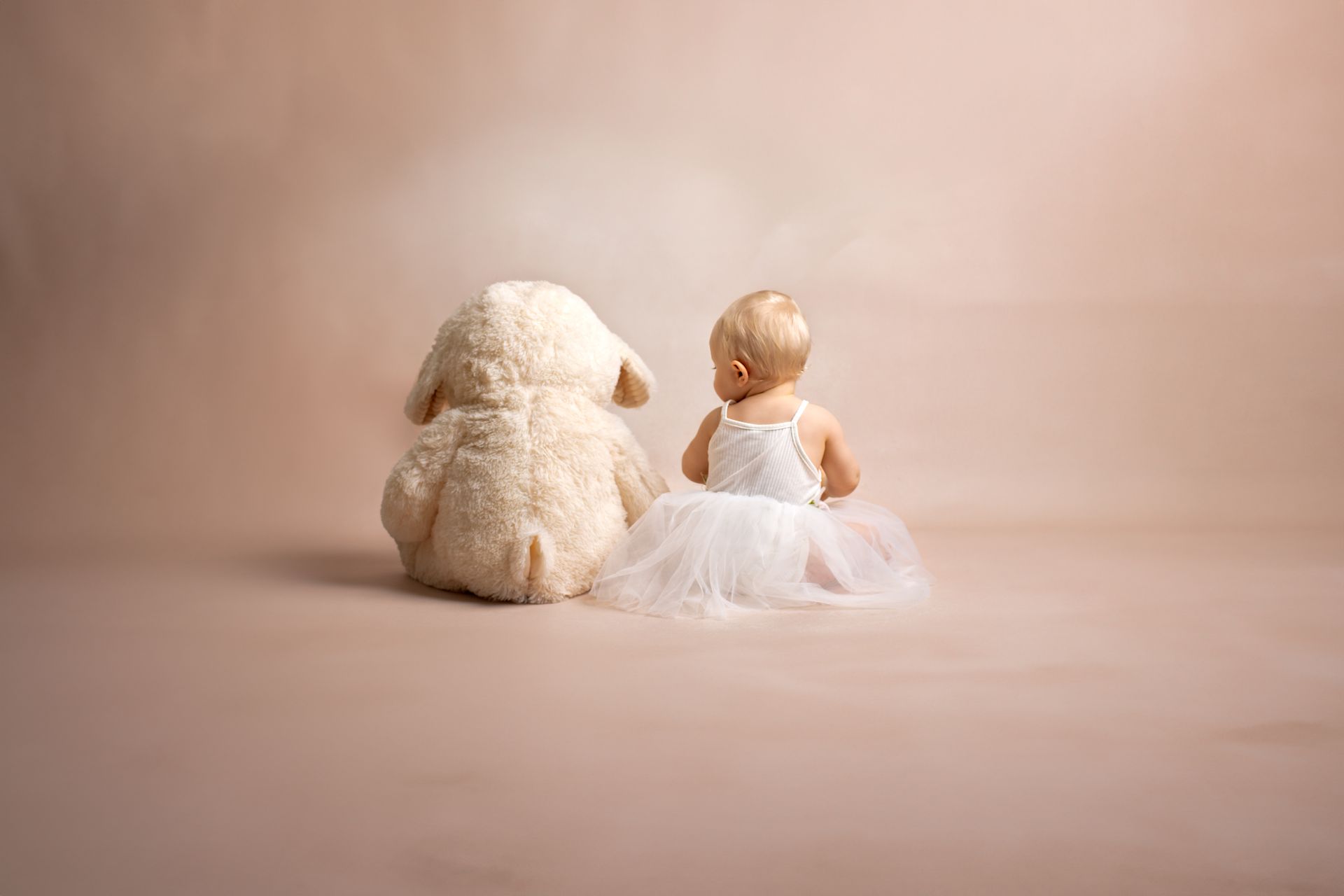 Een babymeisje zit naast een teddybeer.