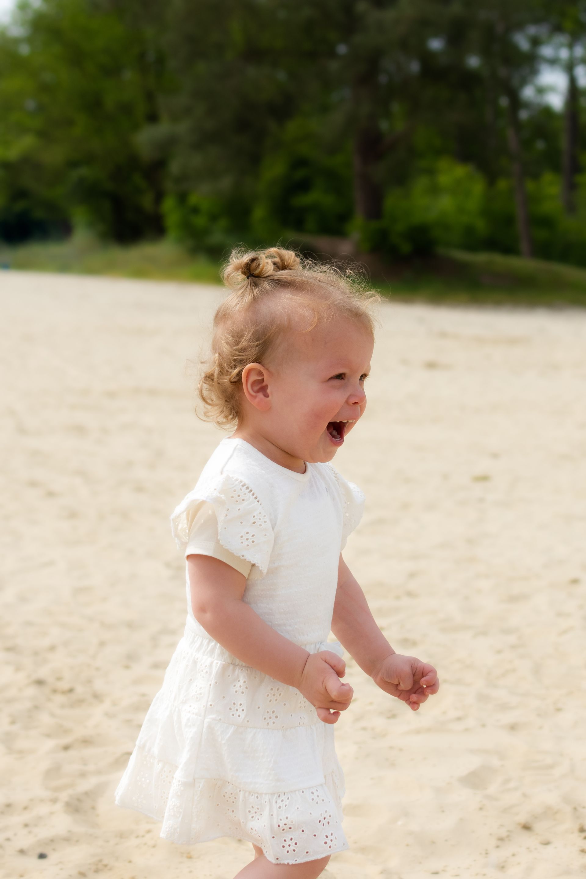 Een klein meisje in een wit jurkje loopt op het strand.