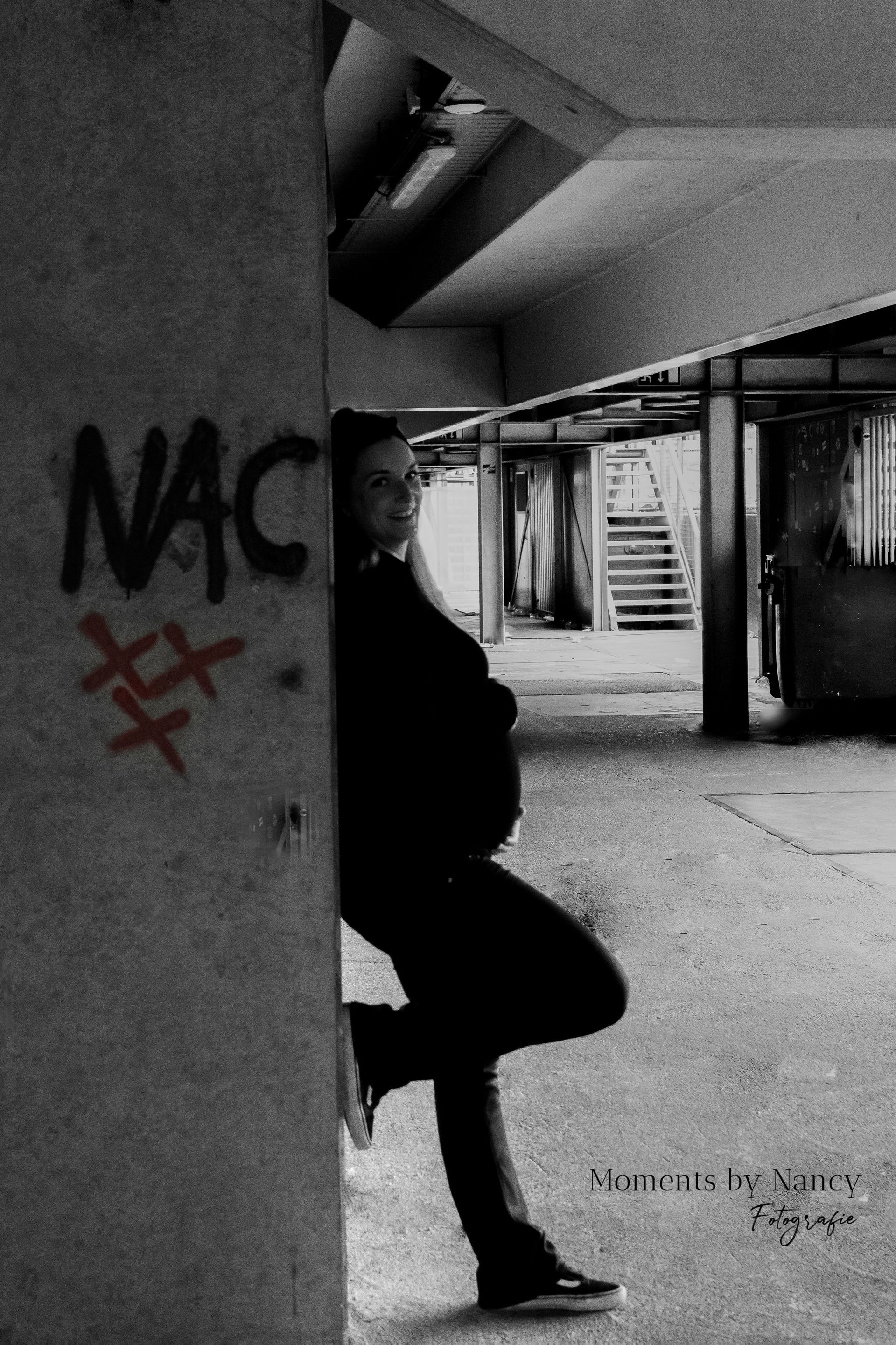 Een zwart-witfoto van een persoon die tegen een muur leunt met het woord NAC erop geschreven