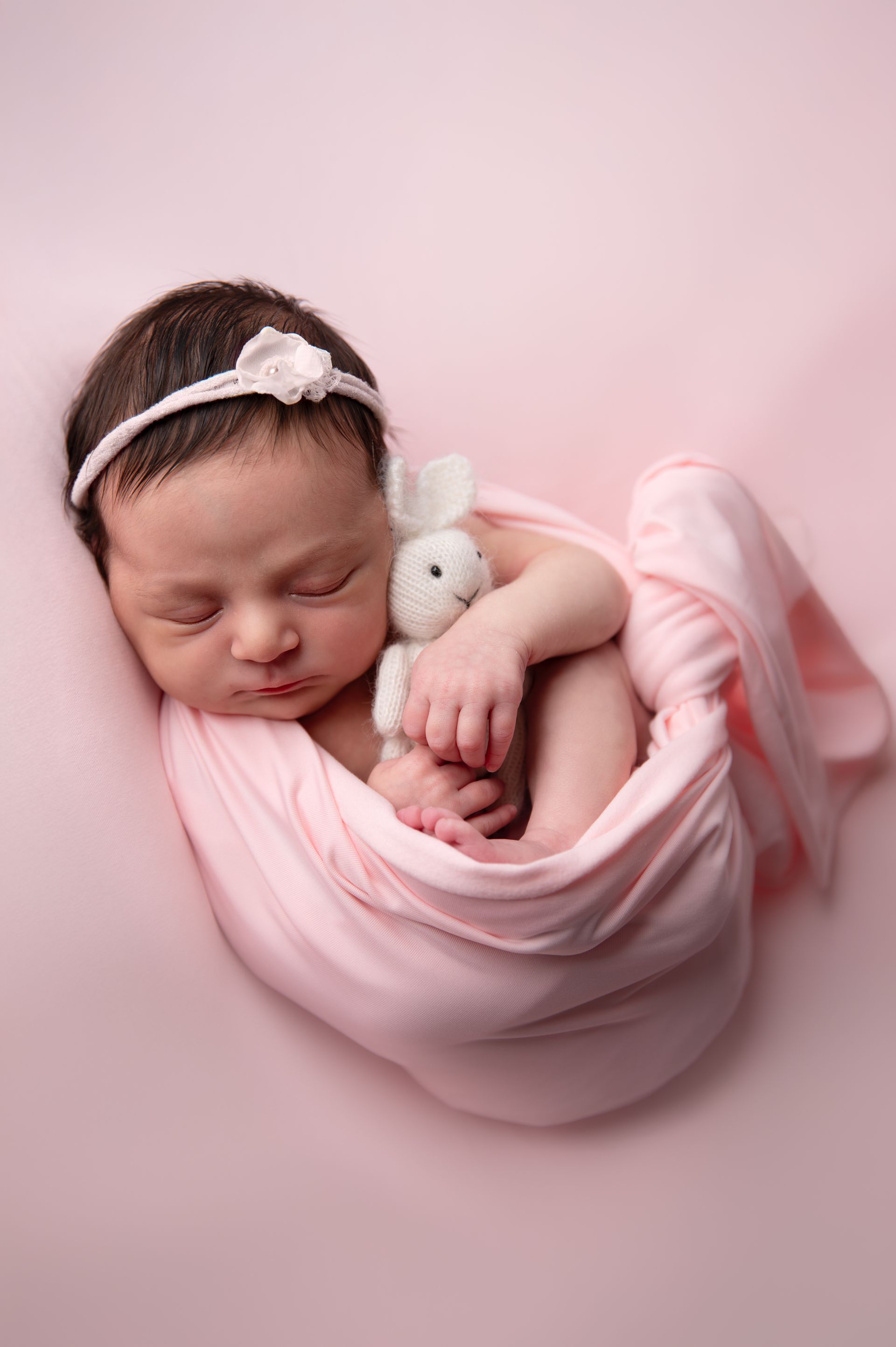Een pasgeboren baby, gewikkeld in een roze deken, houdt een knuffelkonijn vast.