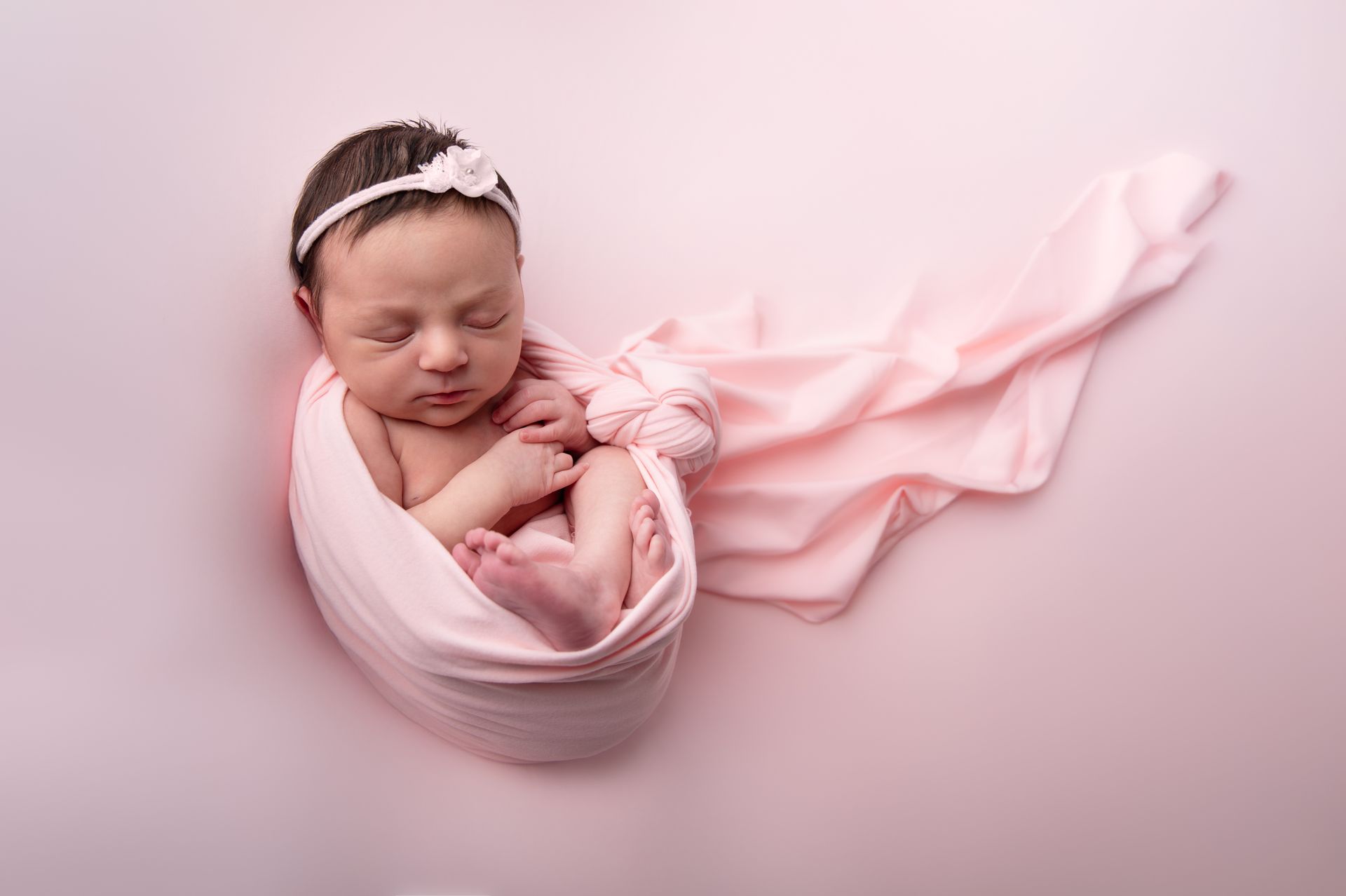 Een pasgeboren baby, gewikkeld in een roze deken, slaapt op een roze achtergrond.