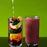 A glass with layered fruits and vegetables next to a filled smoothie glass; liquid pouring into the layered glass.