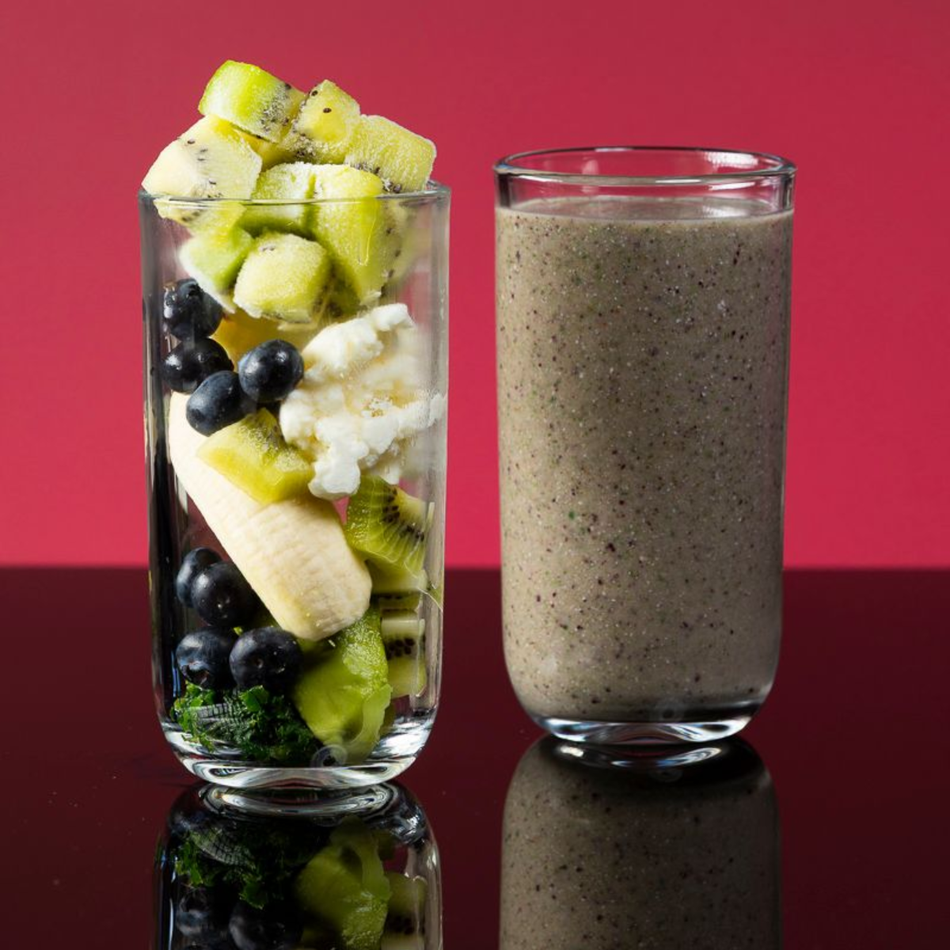 Glass of mixed fruit next to a glass of blended smoothie. Red background.