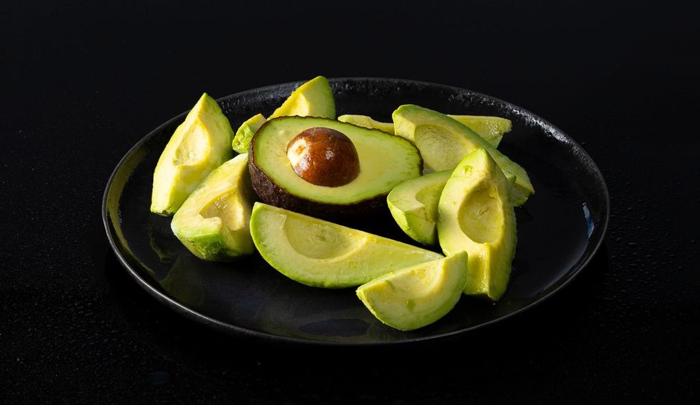 Sliced avocado on a dark plate against a black background.