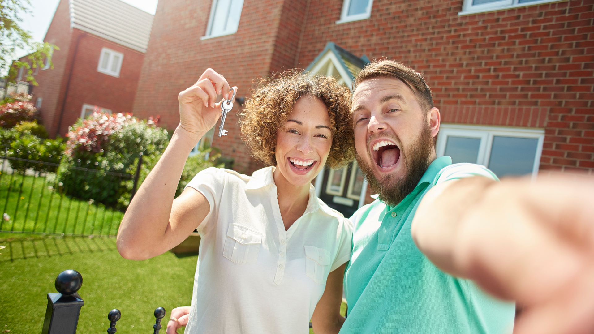 Couple holding keys, smiling in front of new brick house.
