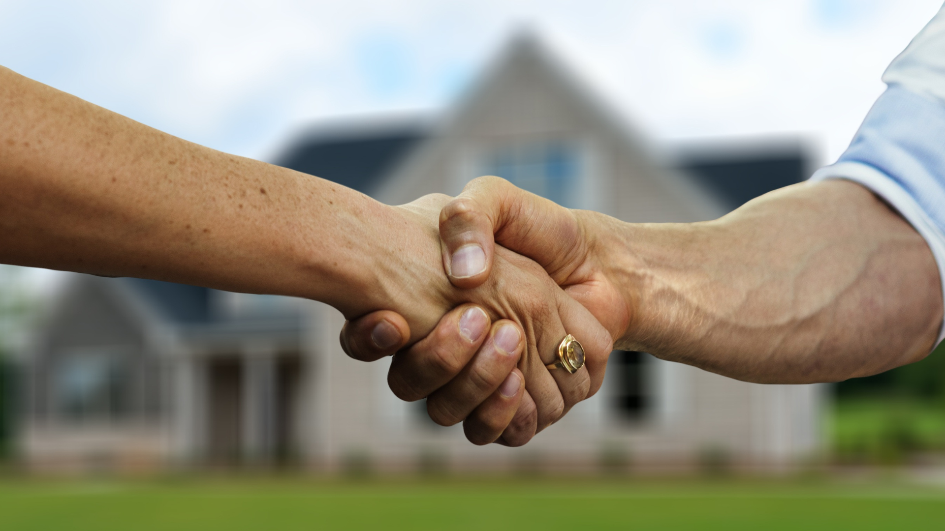 Two people shaking hands in front of a house, symbolizing a real estate deal.