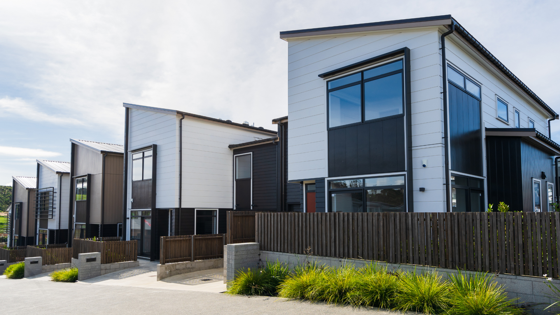Modern row houses with white and black siding, a wooden fence, and blue sky.