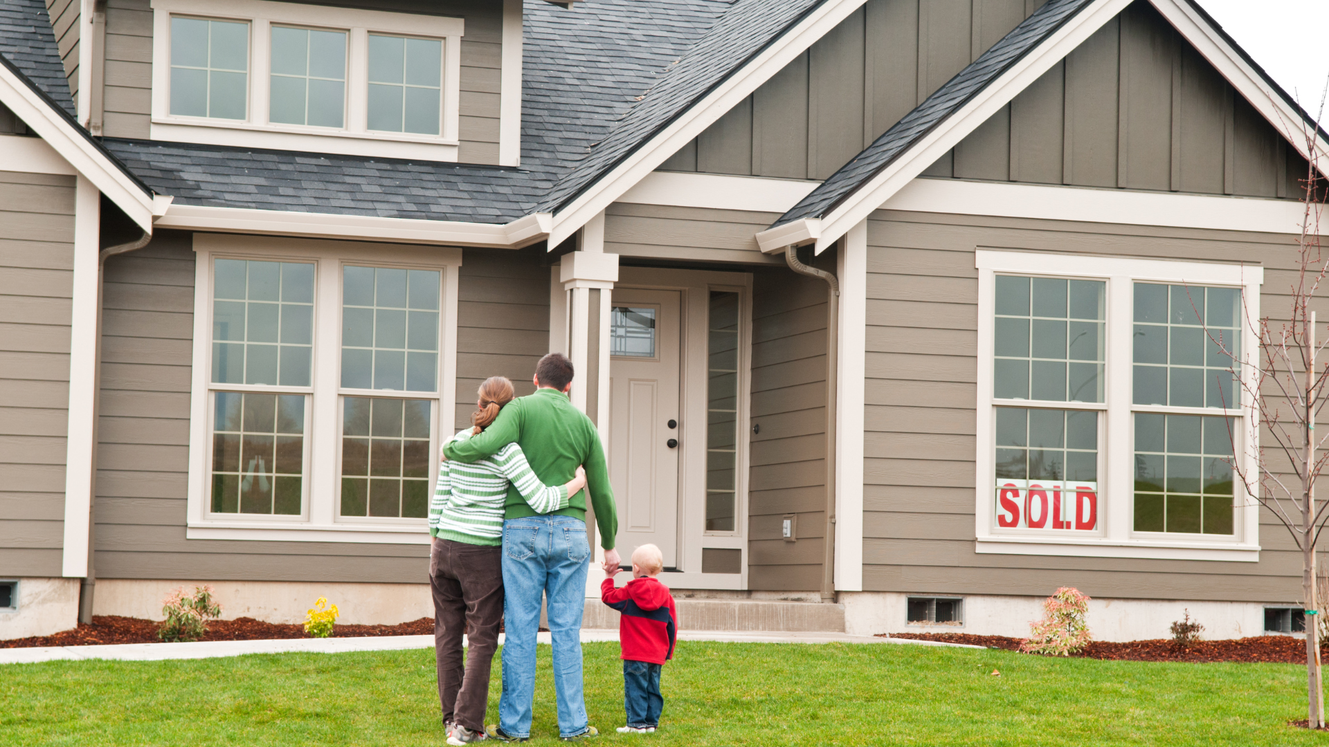 Family of three stands in front of a house with a 