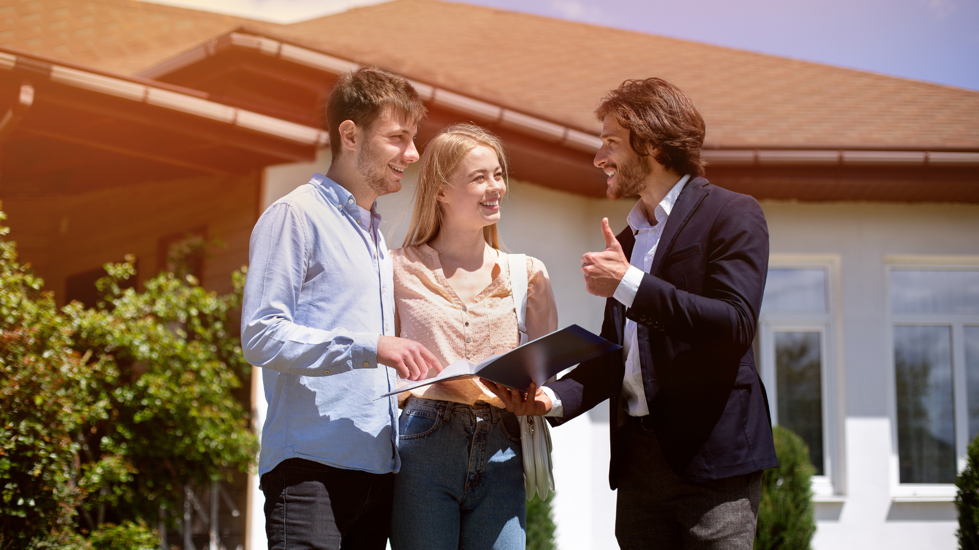 Real estate agent showing documents to a smiling couple in front of a house.