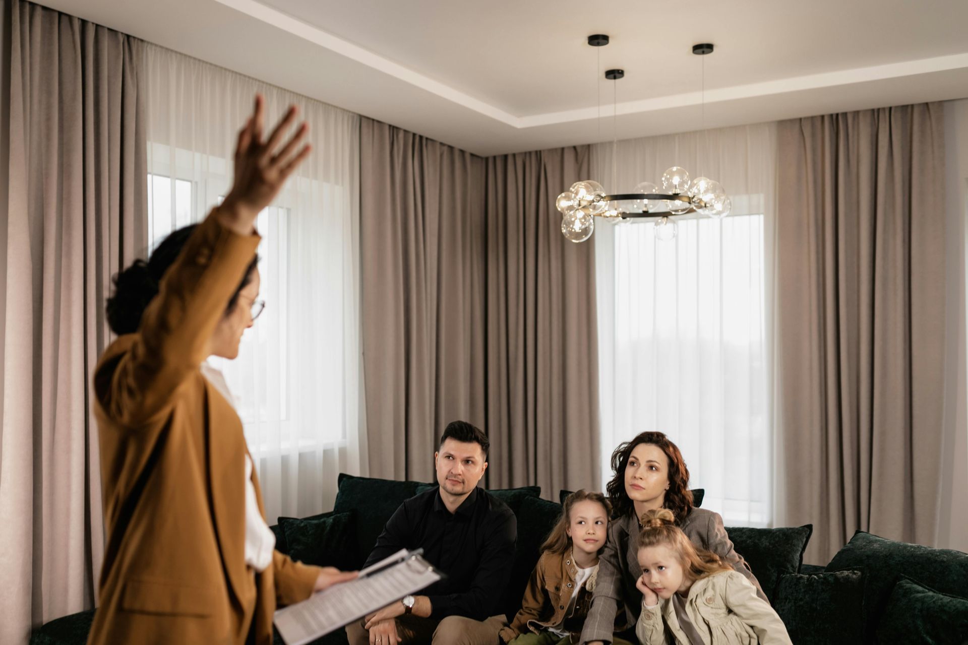 Real estate agent showing home to family, pointing at ceiling. Beige, modern living room.