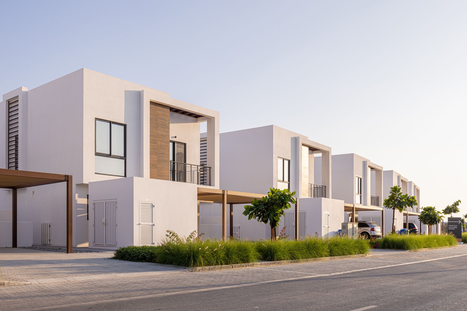 Row of modern white townhouses along a road; clear sky.