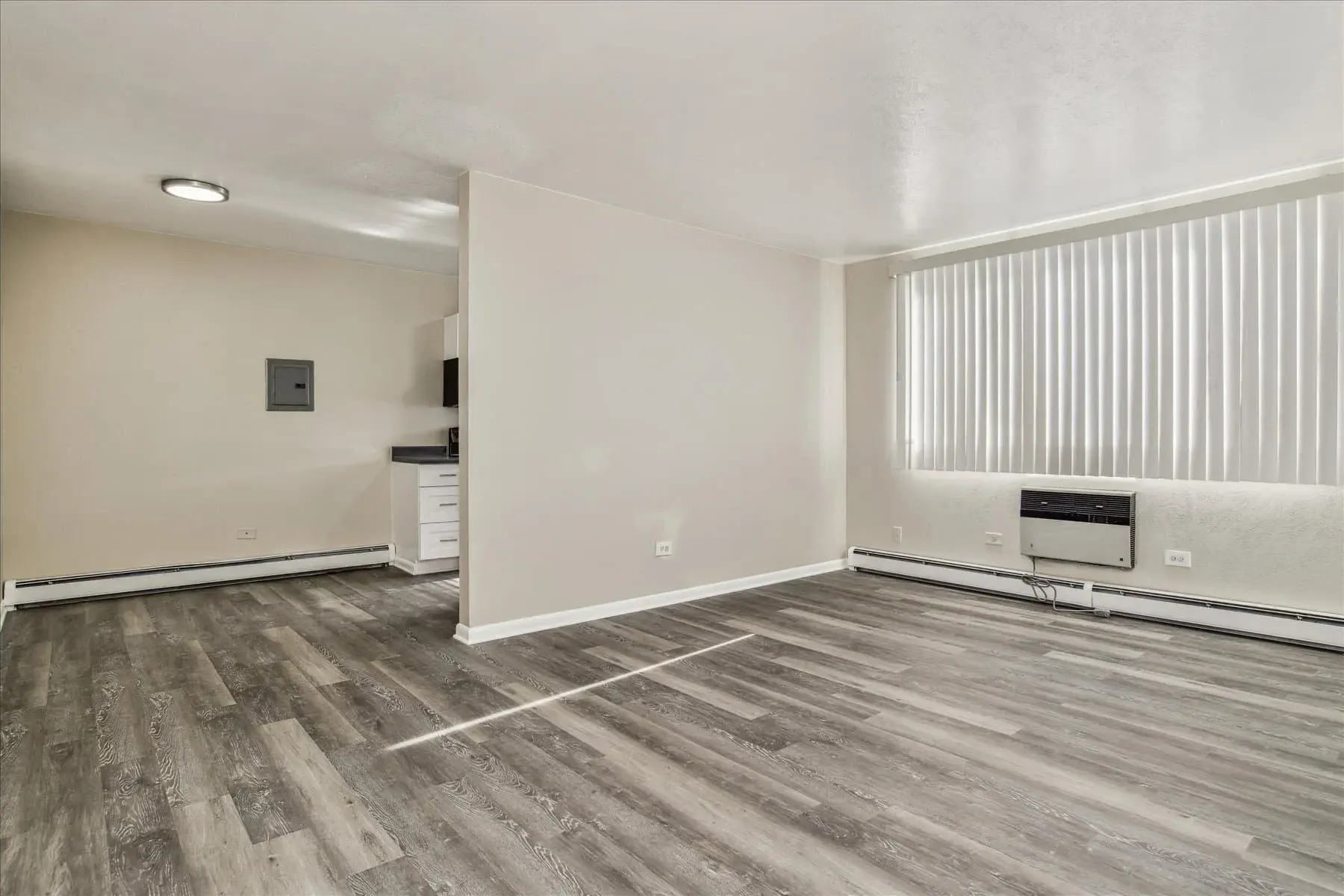 Interior of an apartment with light grey wood-look flooring and white blinds on a large window.