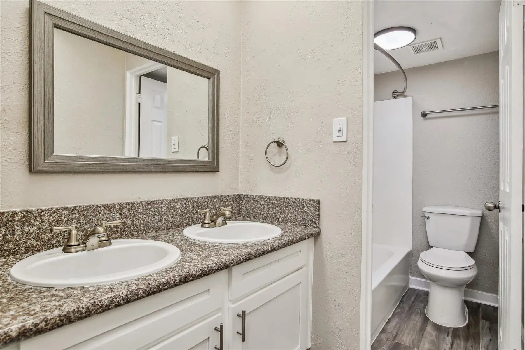 Double vanity with granite countertop and a toilet and bathtub in the background.