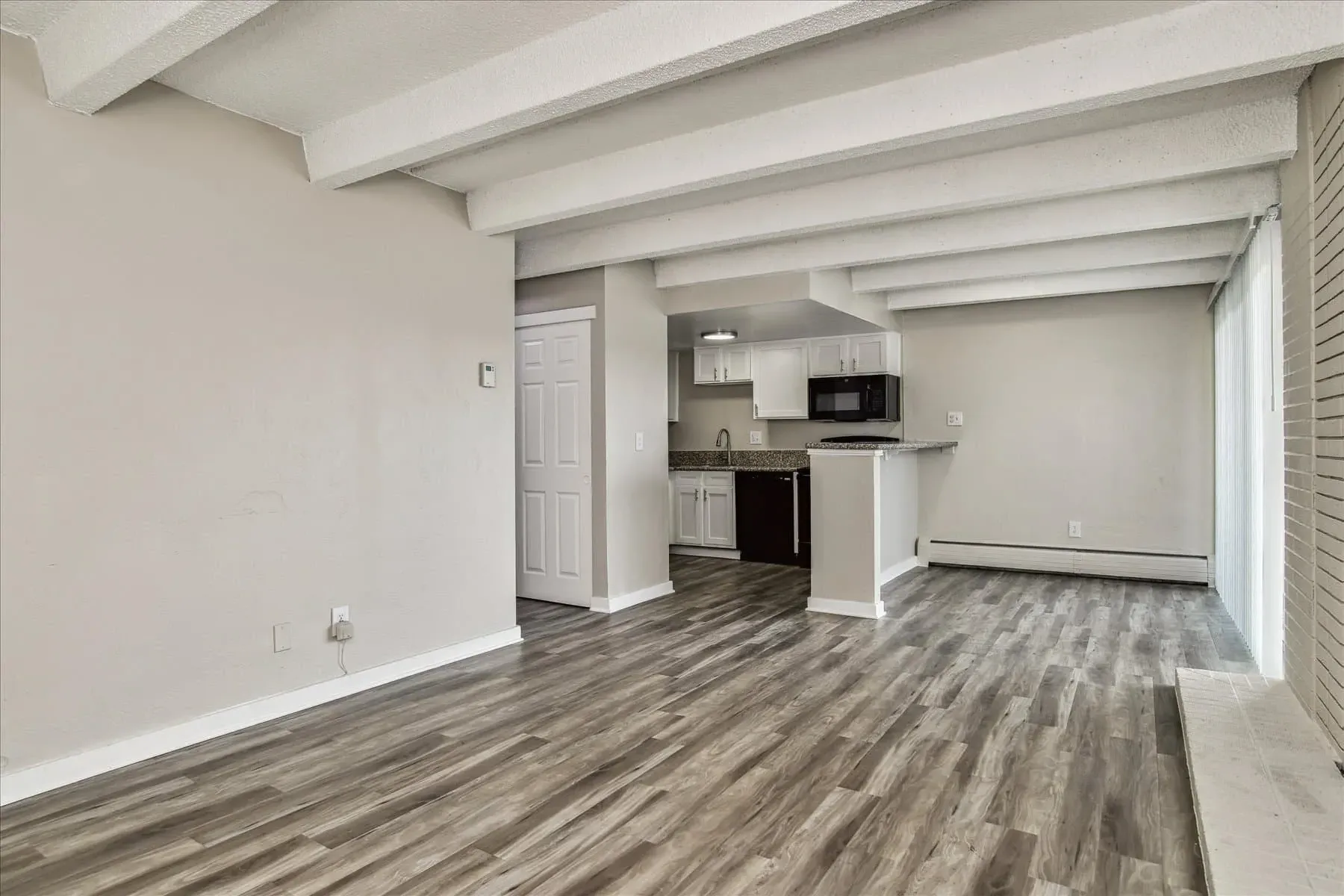 Living room and kitchen area with beamed ceiling and wood-look flooring.